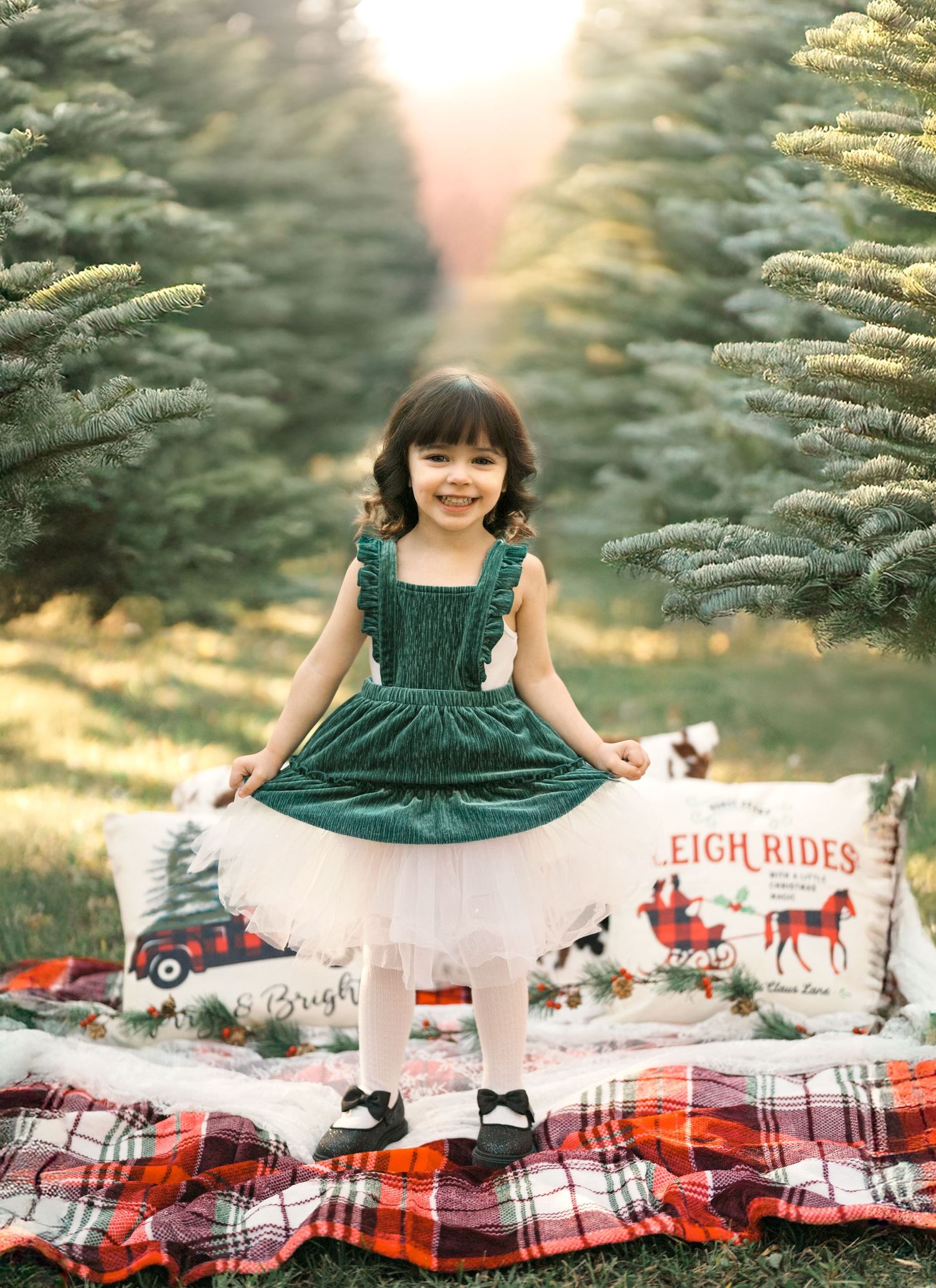 A young girl in chistrmas dress on a festive blanket at a tree farm