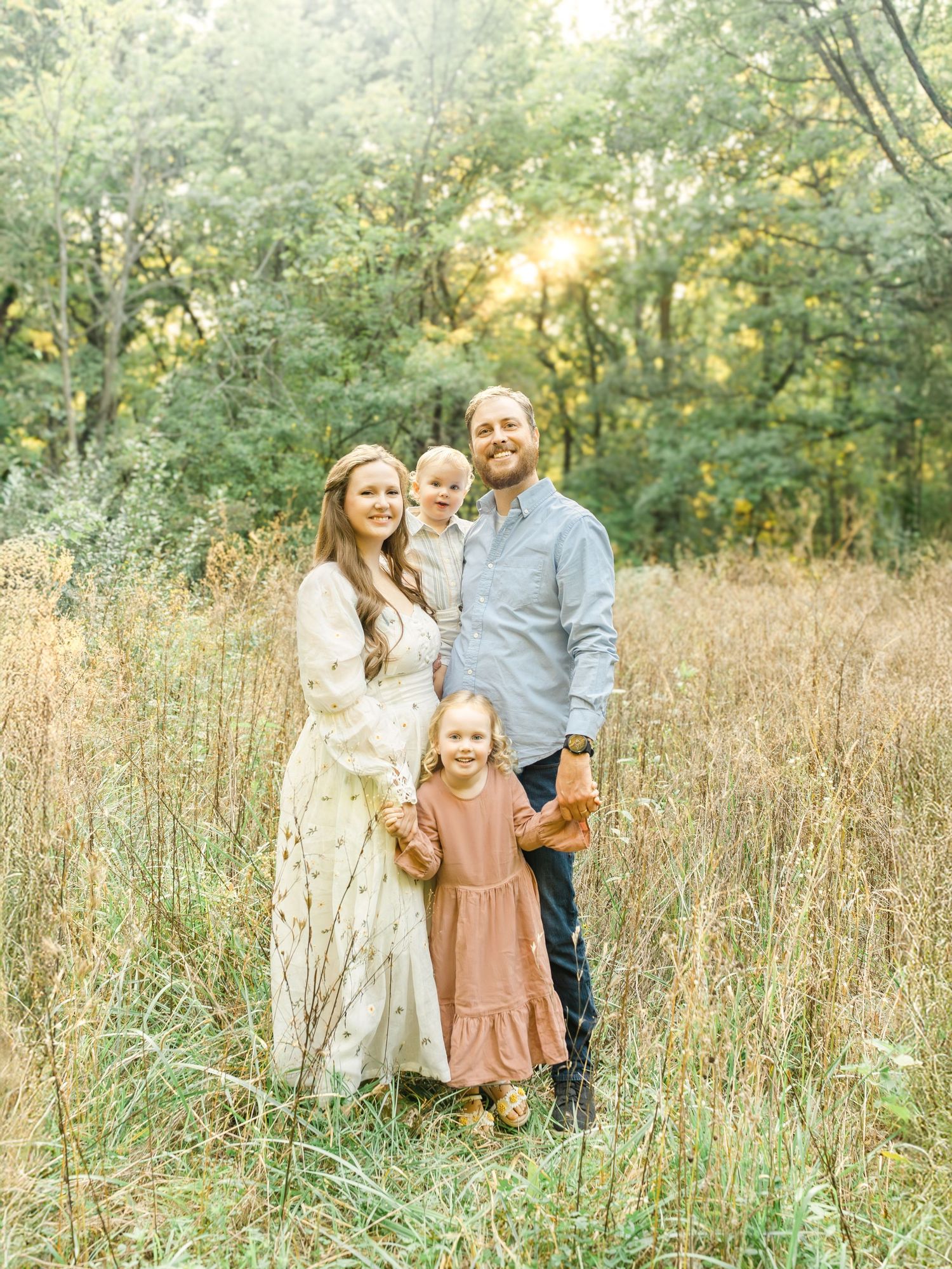 A family of four standing together in tall grass during a golden hour outdoor photo session in Kansas City.