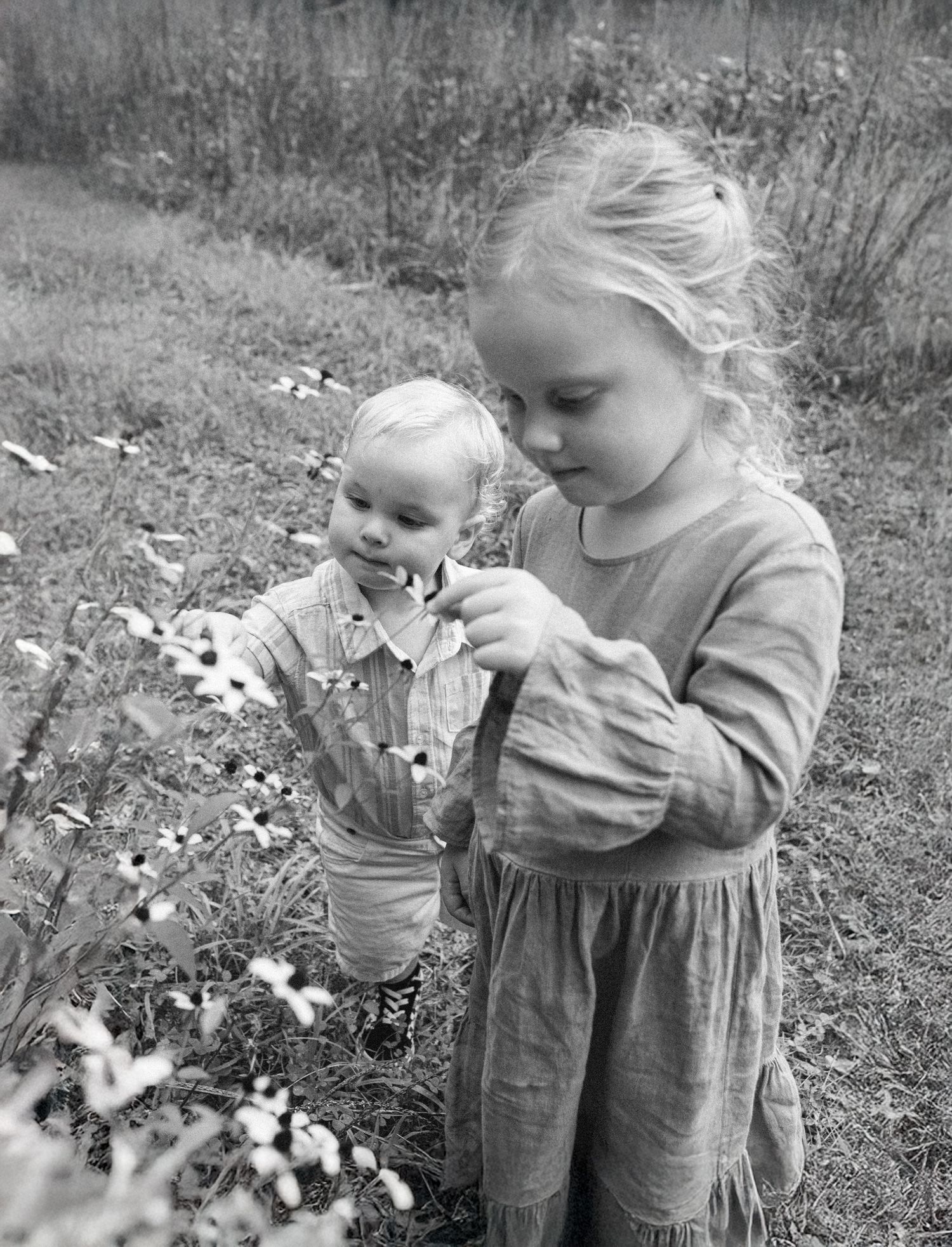 Two young siblings holding flowers together during an outdoor family session, captured in black and white.