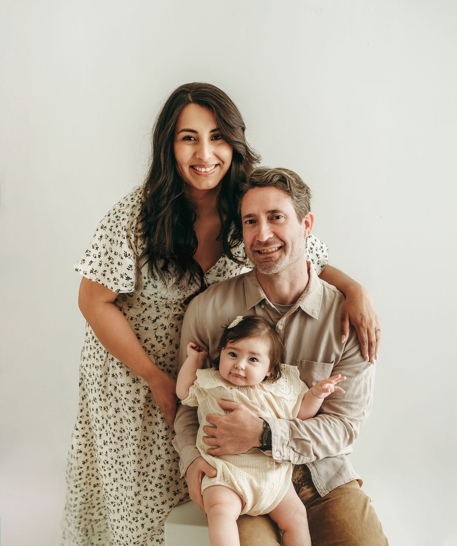 Parents sitting with their baby girl during a soft, neutral family photo session in a studio.