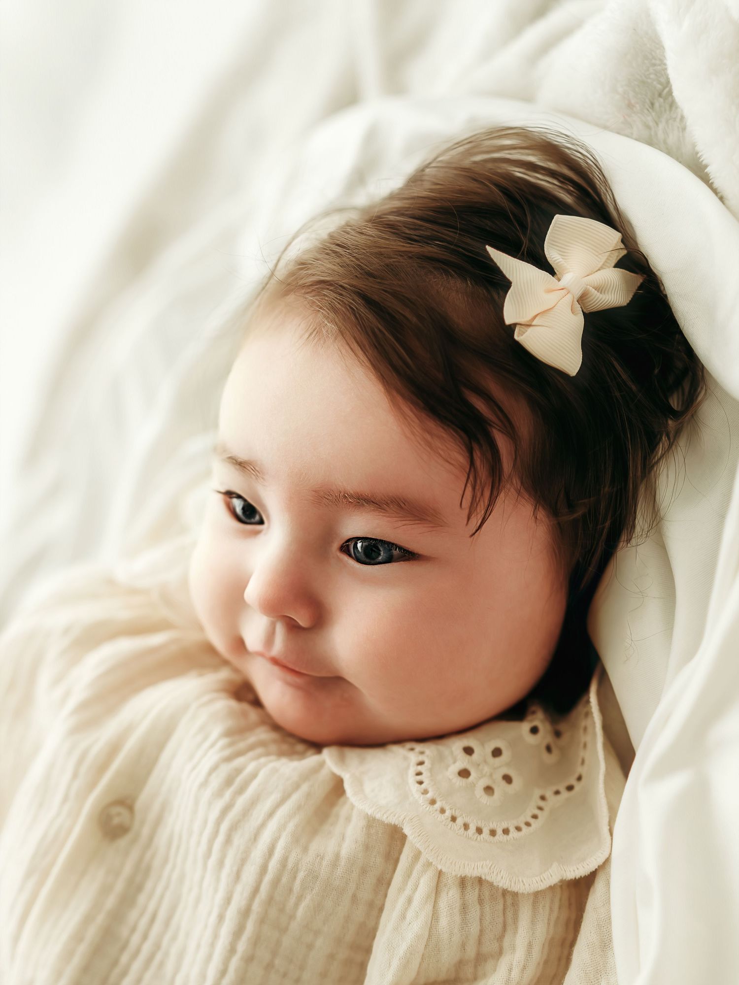 A baby girl looking off to the side while lying on a soft neutral blanket during a studio session.