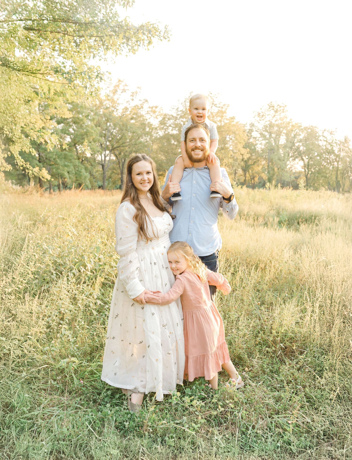 A family of four standing close together in a grassy field during a golden hour outdoor photo session in Kansas City.