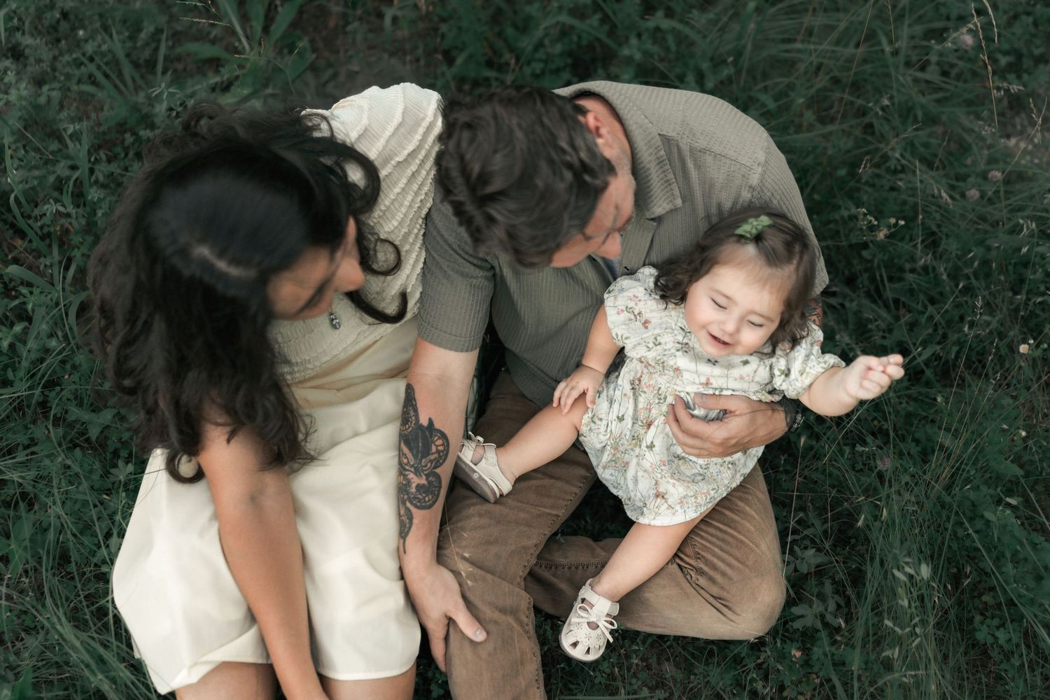 Overhead view of parents laughing with their daughter while sitting together in the grass.