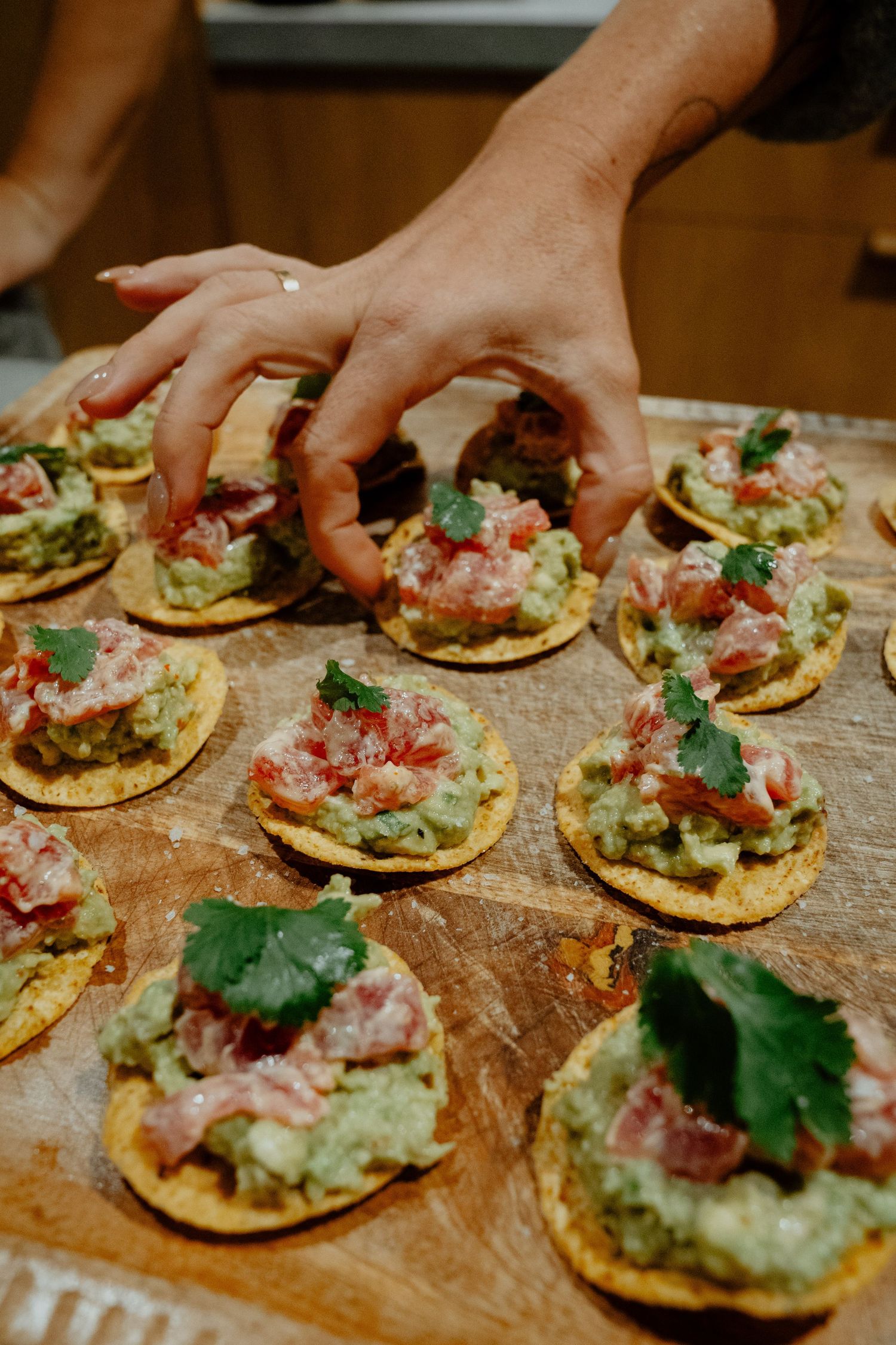 Hands arranging guacamole and tuna tartare appetizers on crispy crackers.