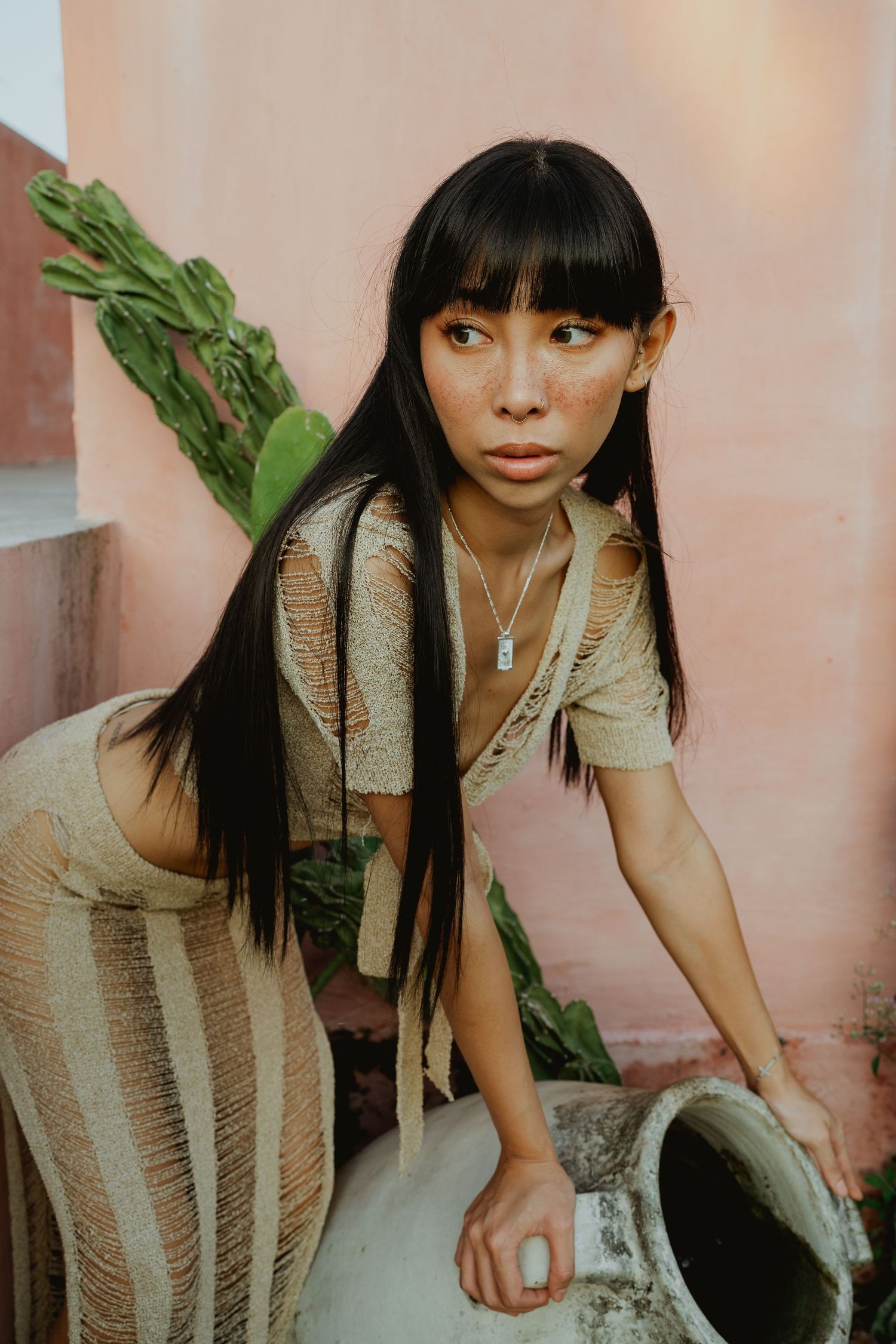 Young Asian woman with long black hair posing near a cactus in a beige knit outfit.