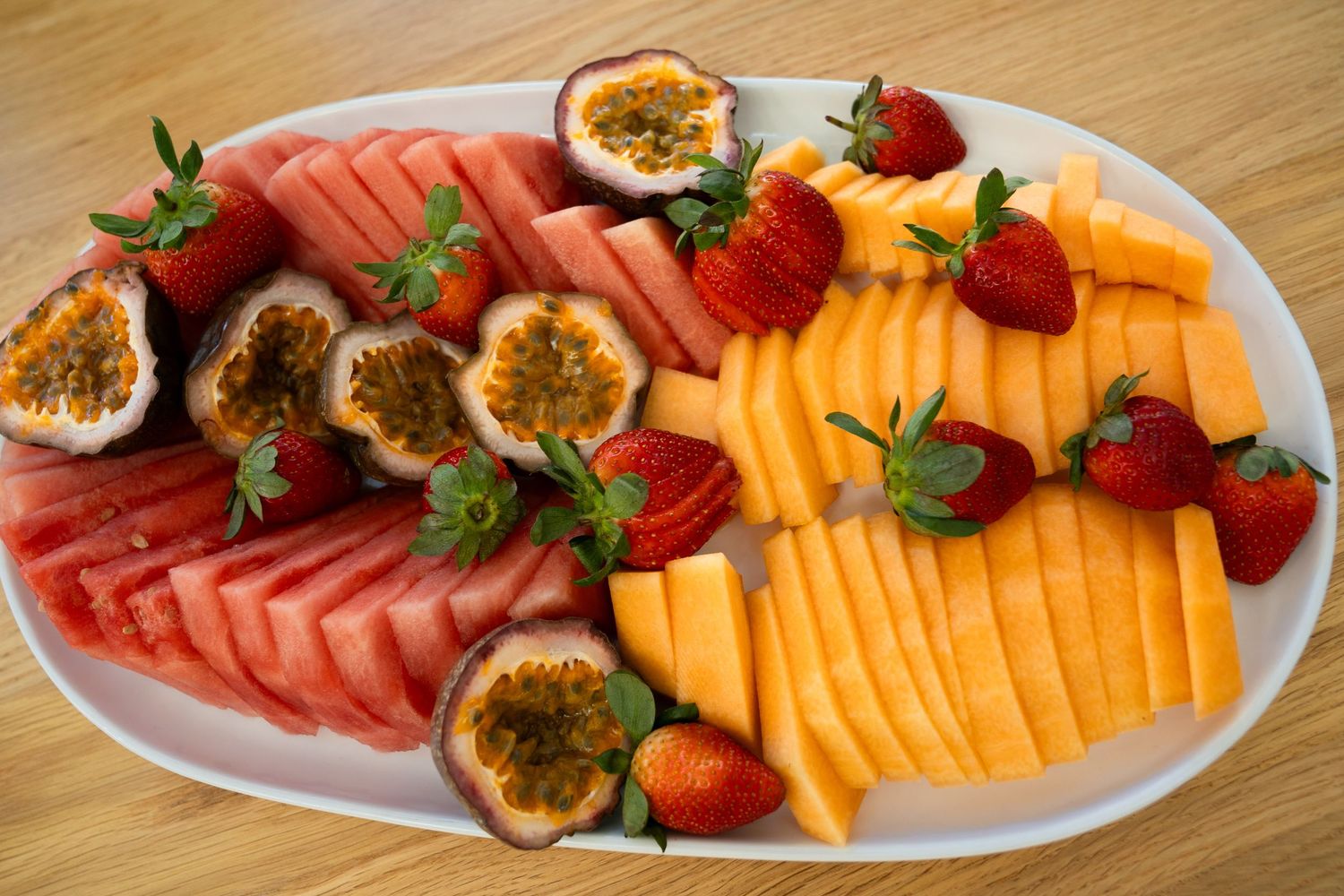 Fresh fruit platter with watermelon, mango, strawberries, and passion fruit on a white oval plate.