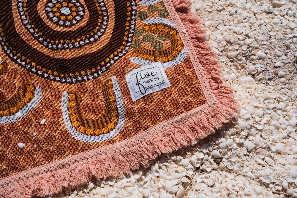 Close-up of brown Aboriginal dot art beach towel with pink fringe trim and logo tag.