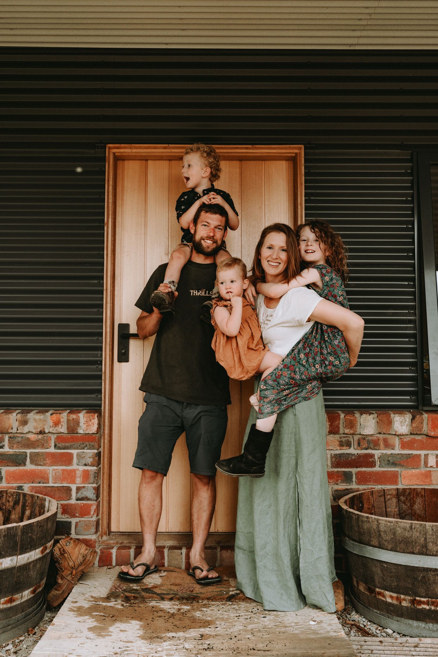 Happy family of five posing at front door with children on shoulders and in arms.