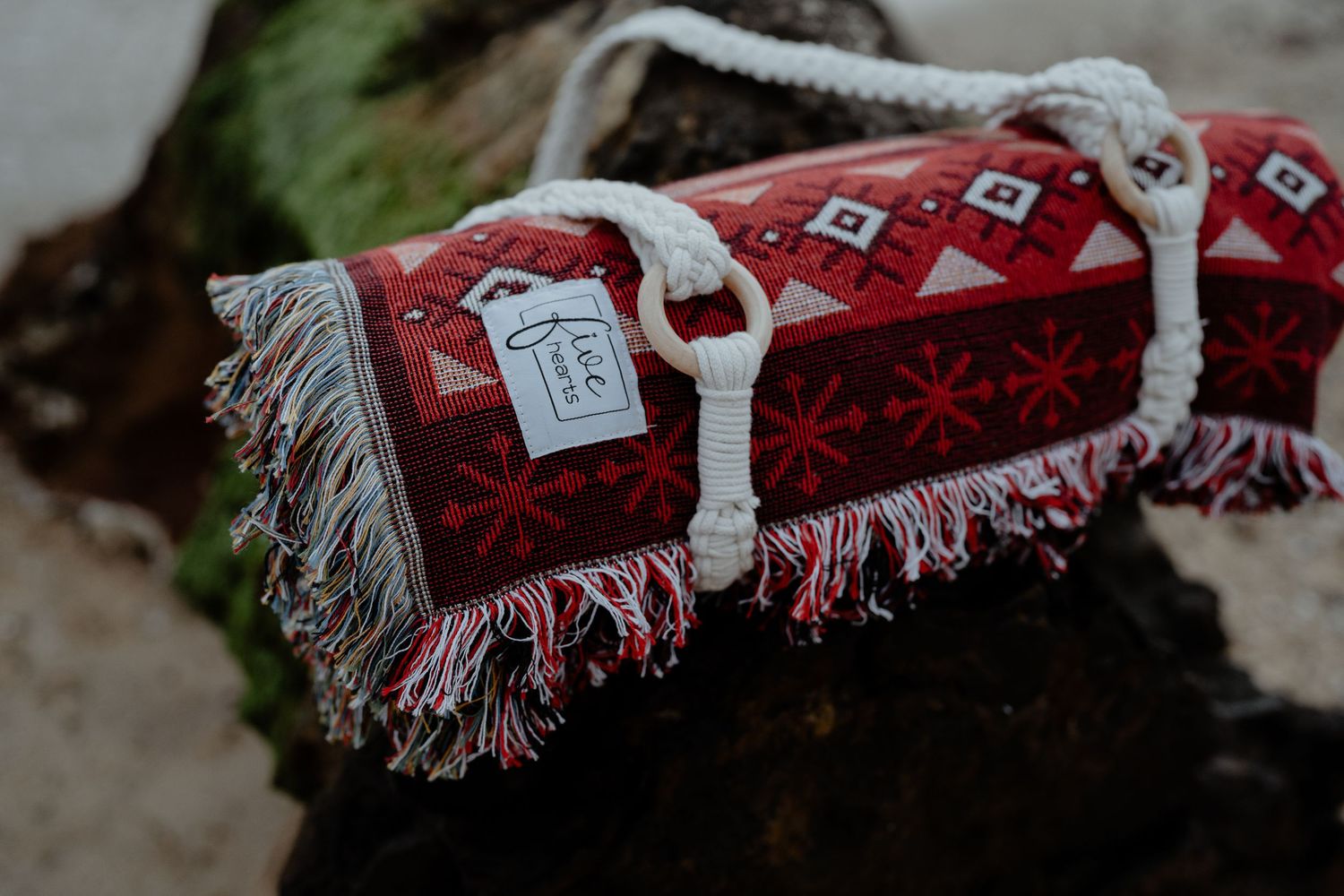 Rolled red Nordic patterned blanket with fringe tied with rope on a rustic wooden surface.
