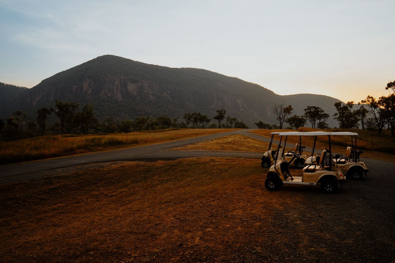 Two golf carts parked on a dirt path at sunset with a dramatic mountain backdrop.