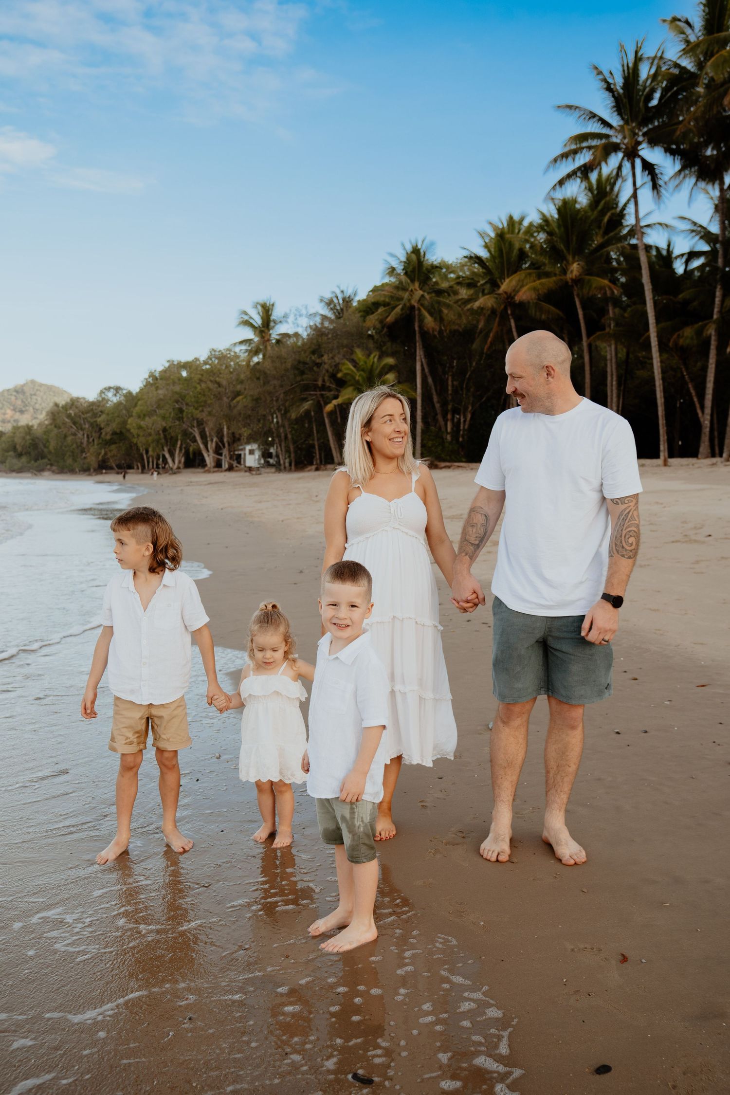 Family of five in white outfits walks hand in hand on tropical palm beach.