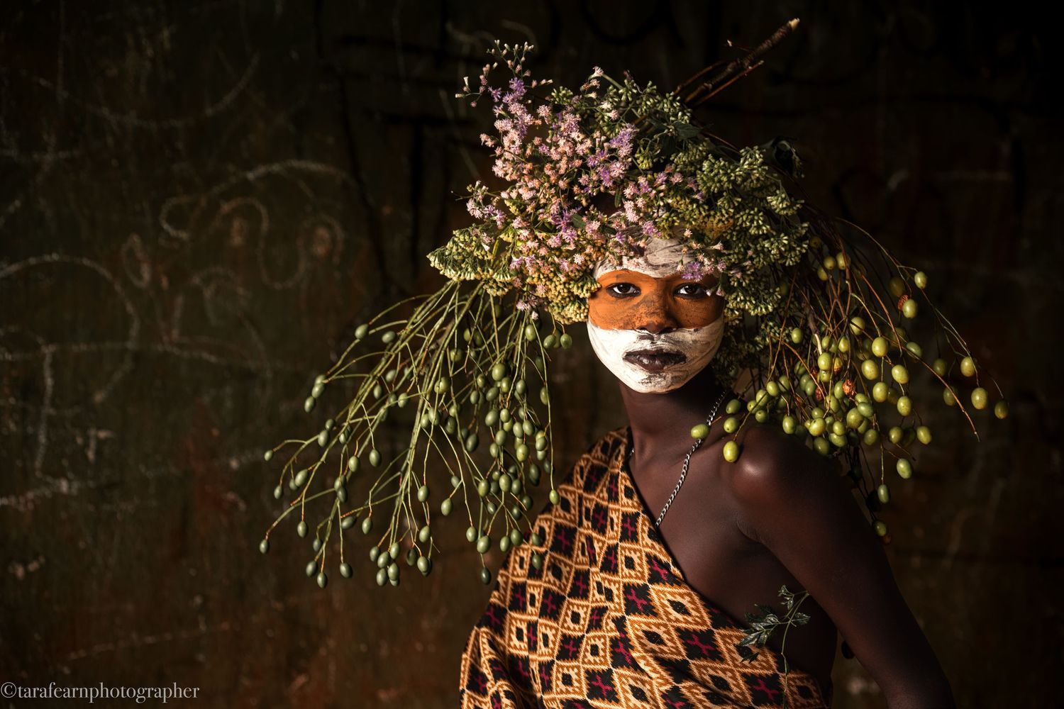 Portrait of an African child wearing an elaborate floral headdress with face paint in warm light.