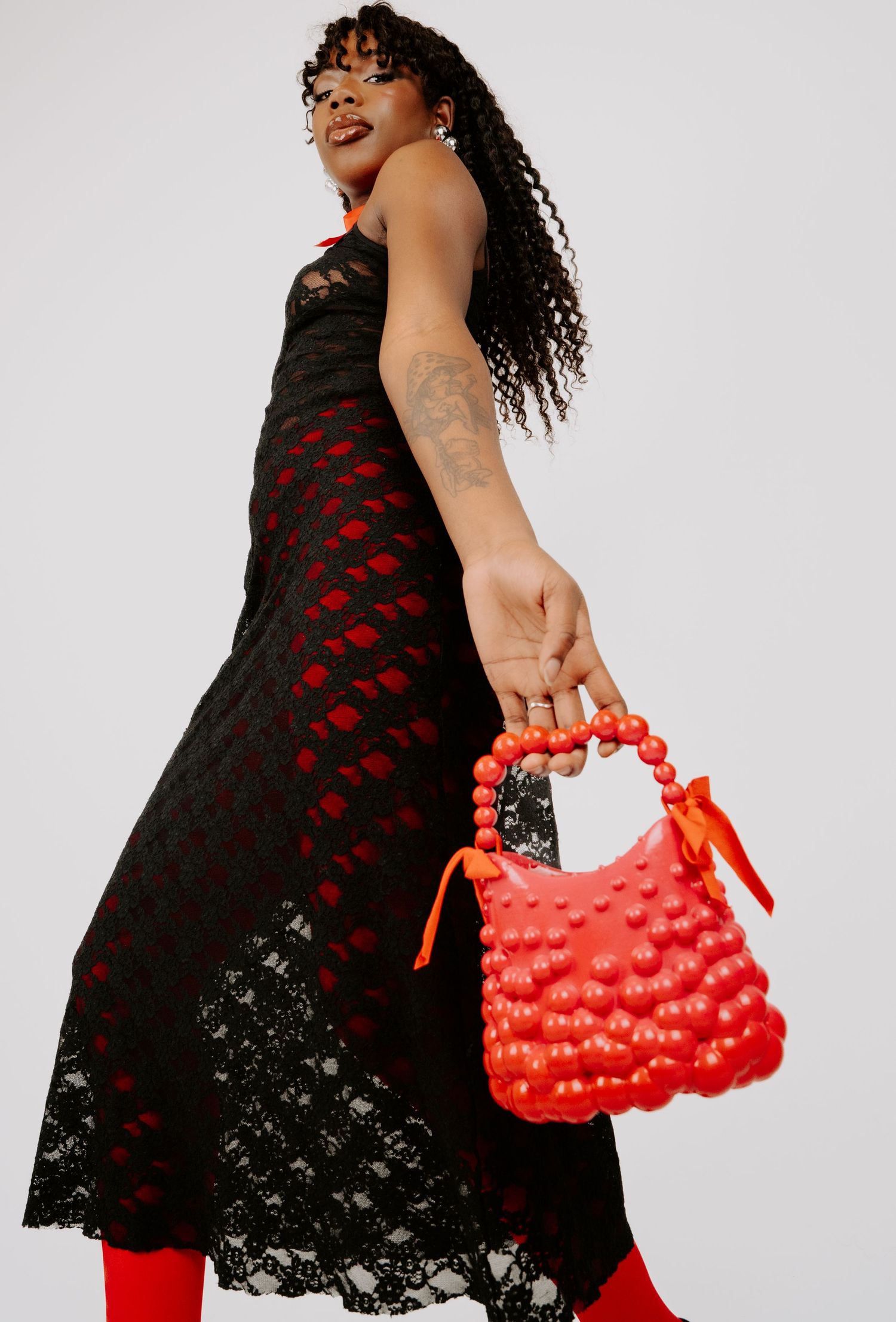 Model in black lace dress holding red beaded handle bubble-textured handbag with bow.