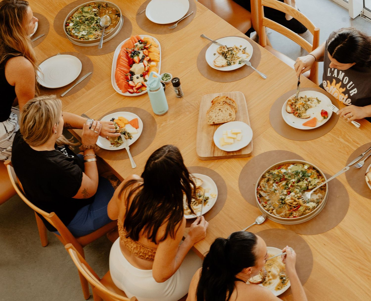 Women sharing a healthy meal together at a wooden dining table with colorful dishes.