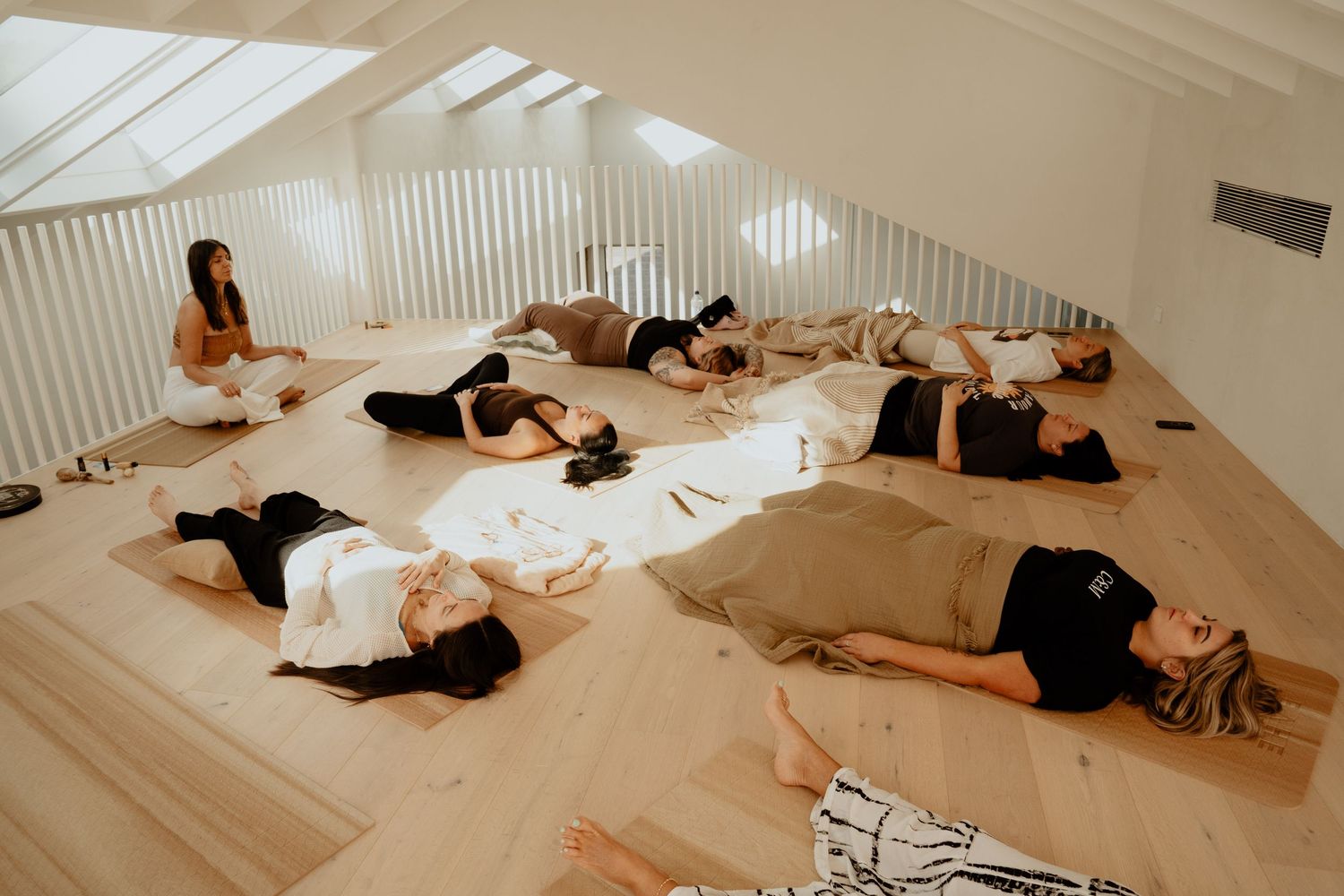 Group of women lying on yoga mats during a relaxation session in a bright attic studio space.