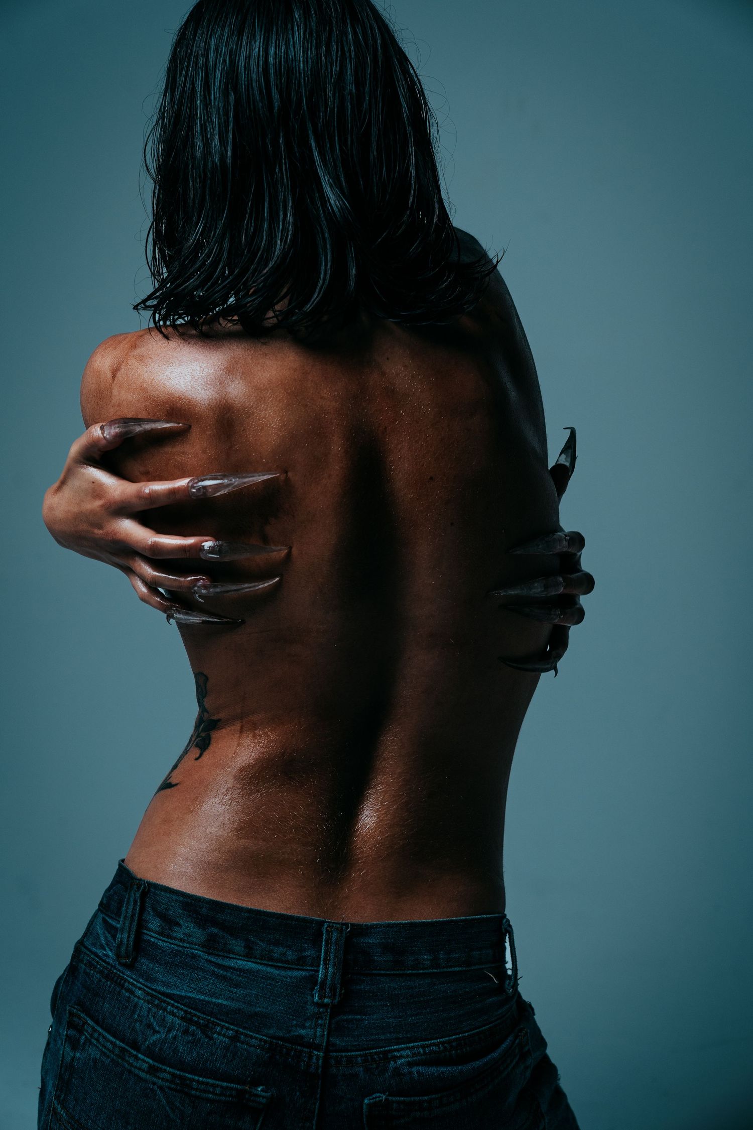 Back view of a woman with wet hair in jeans, arms crossed over her bare back on blue background.