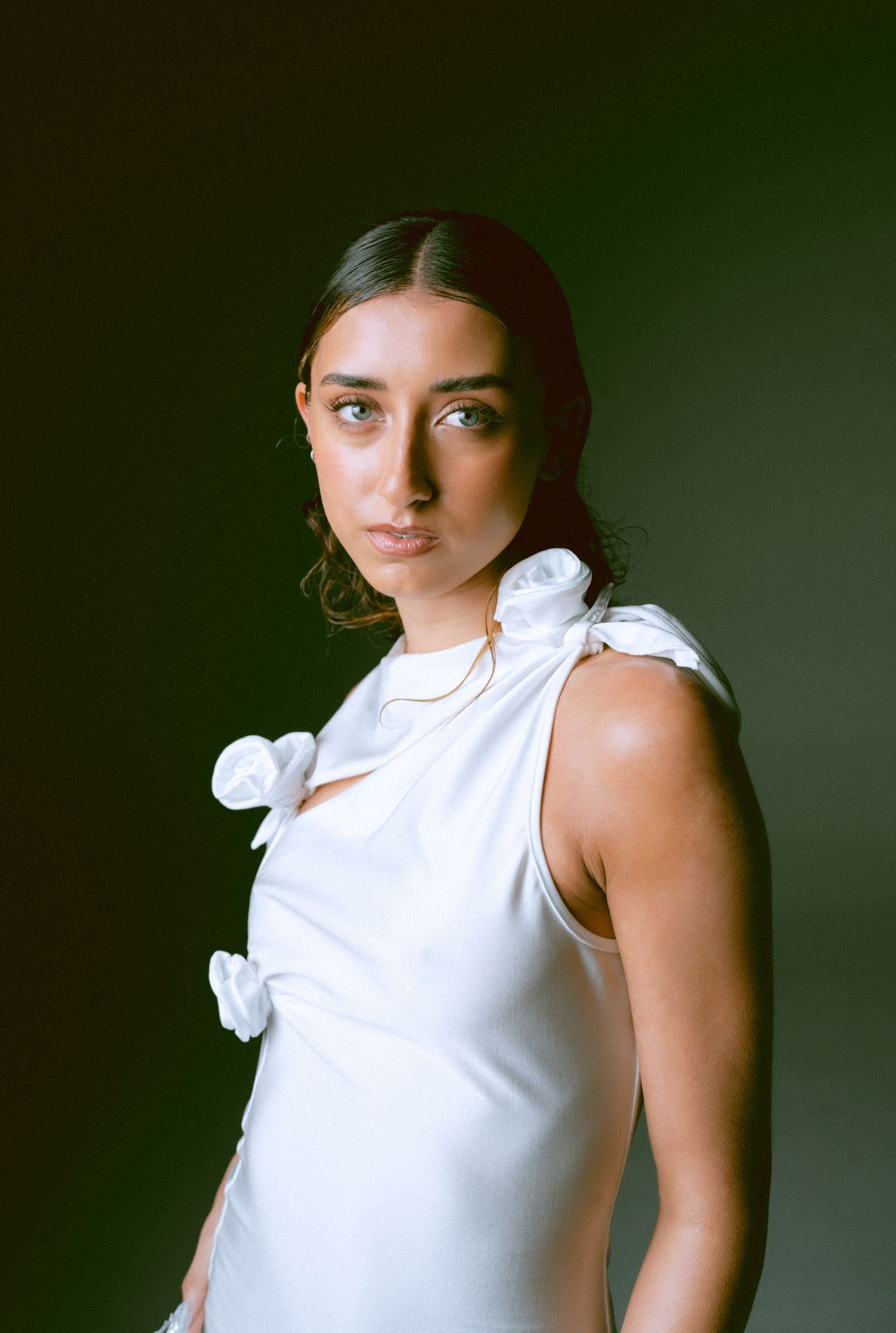 Woman in white floral sleeveless dress posing against dark green studio background.