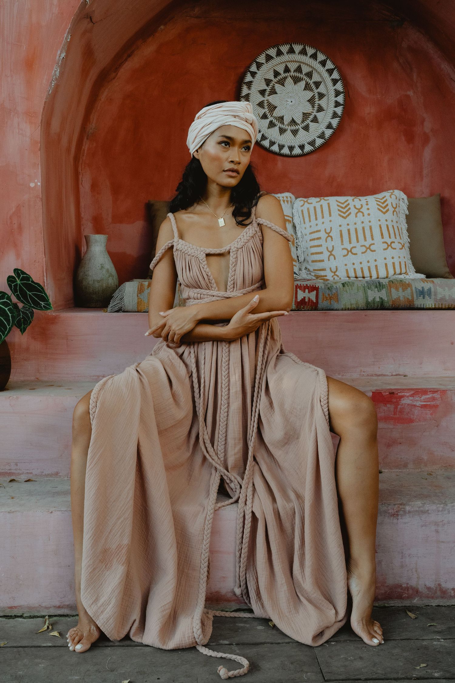 Woman in beige pleated dress and white turban seated in Moroccan alcove.
