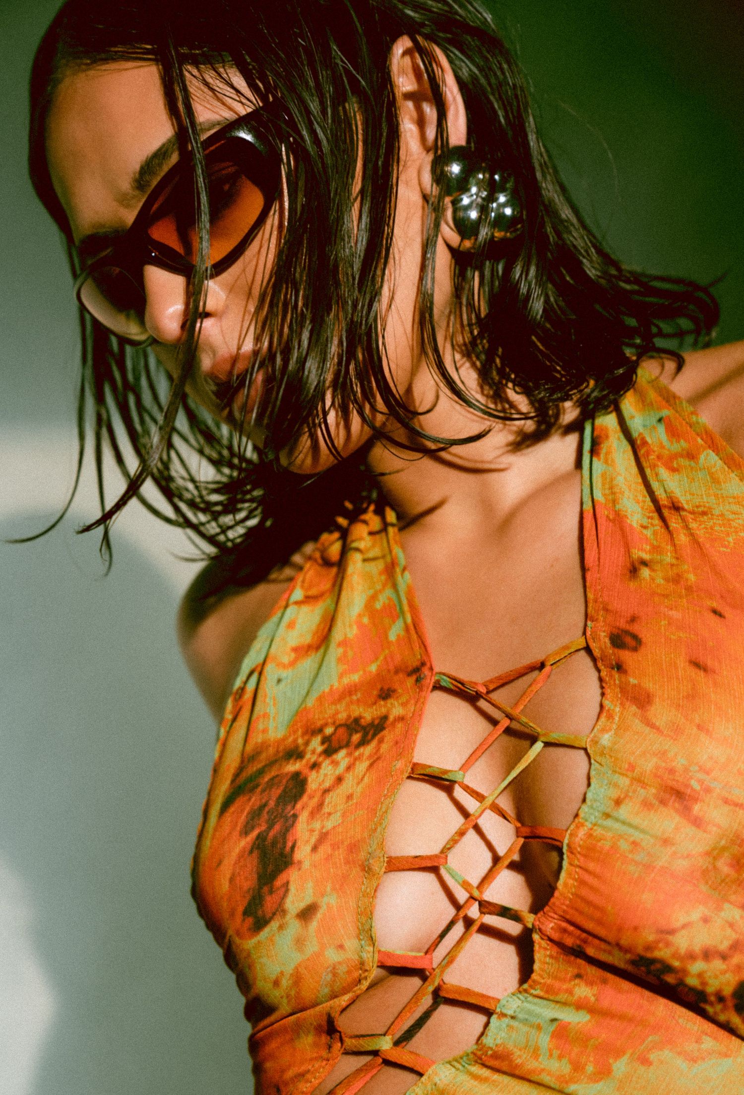Woman in orange tie-dye lace-up halter top with large earrings and sunglasses in sunlight.