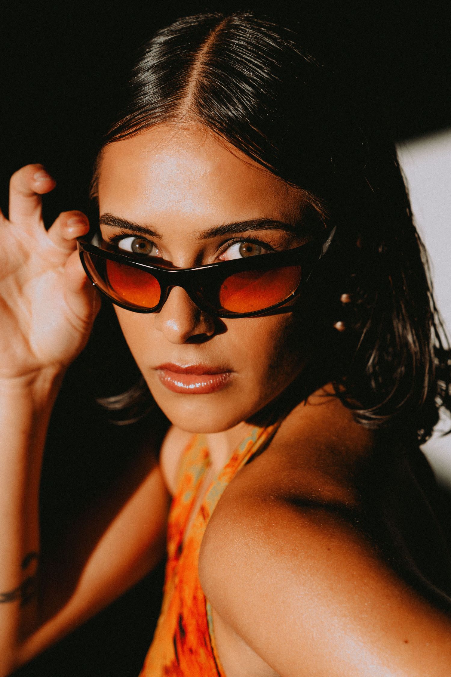 Close-up of woman wearing brown gradient oval sunglasses in warm dramatic lighting.