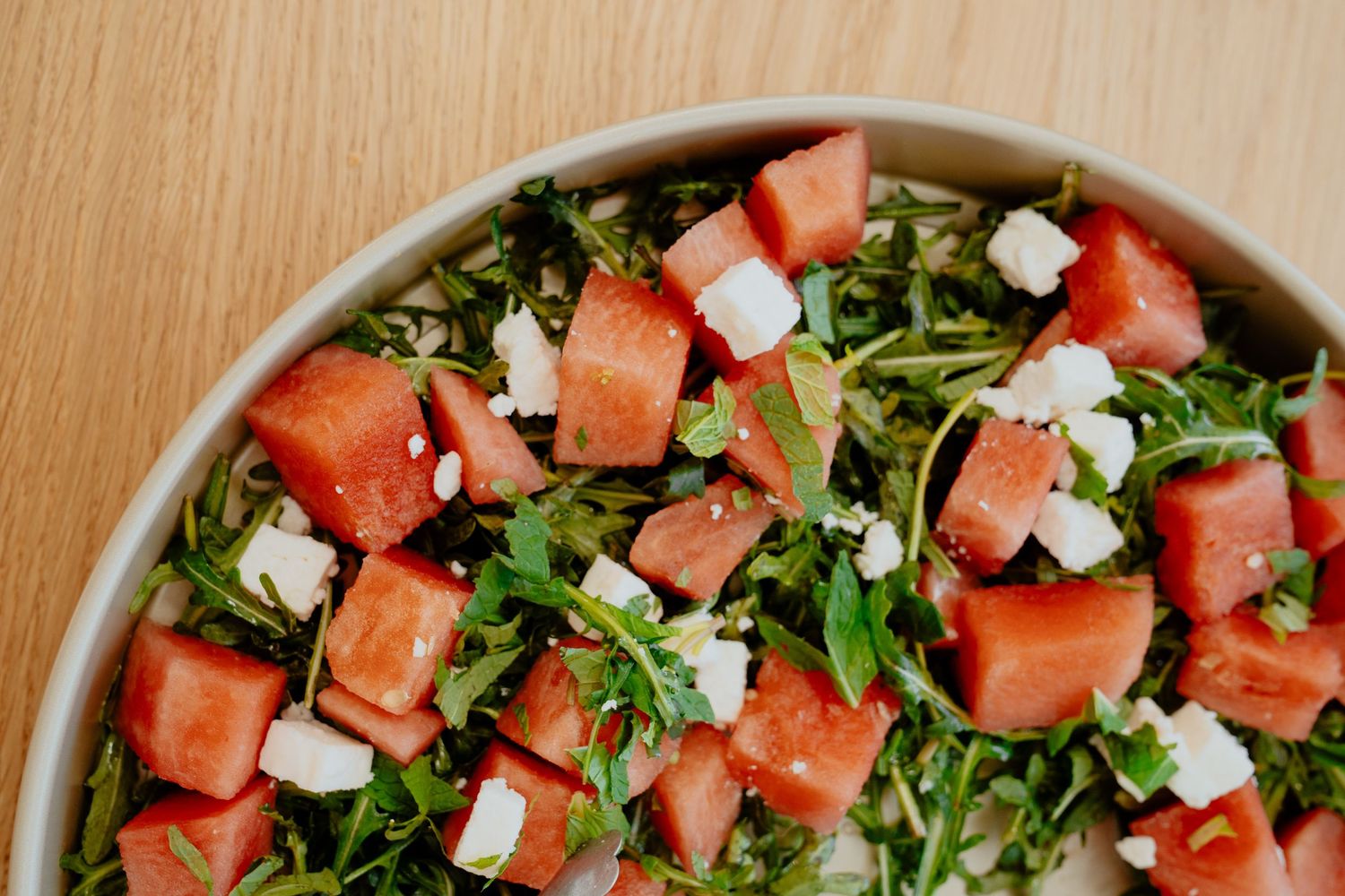 Fresh watermelon salad with arugula and crumbled feta cheese in a large bowl.