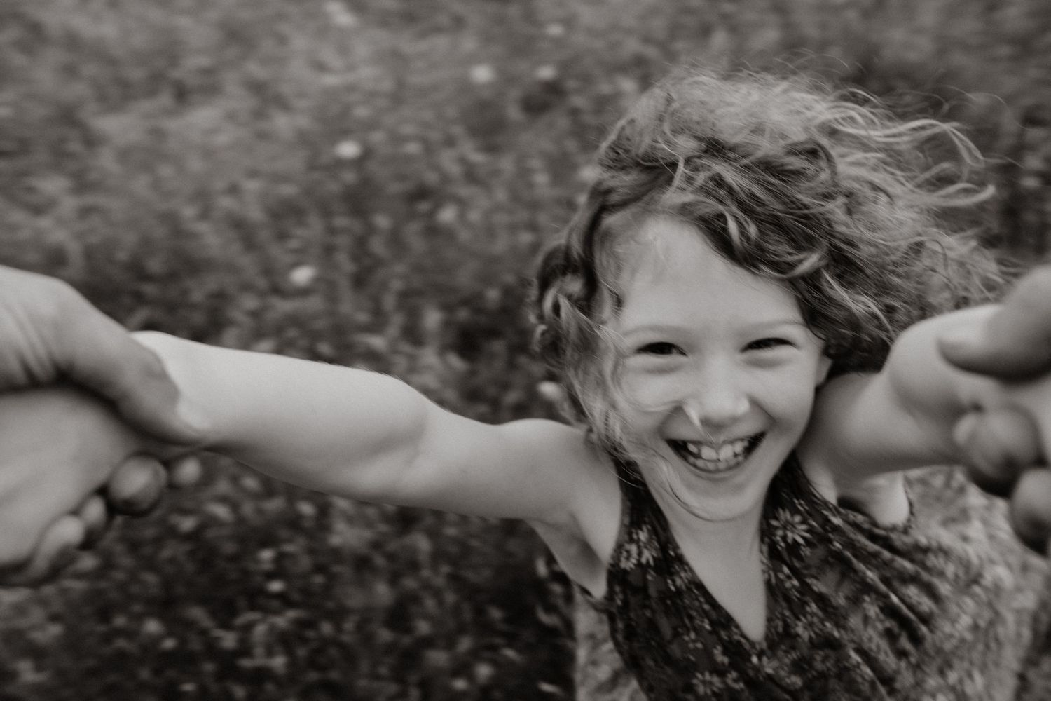 Joyful girl with curly hair laughing and reaching toward camera in black and white photo.