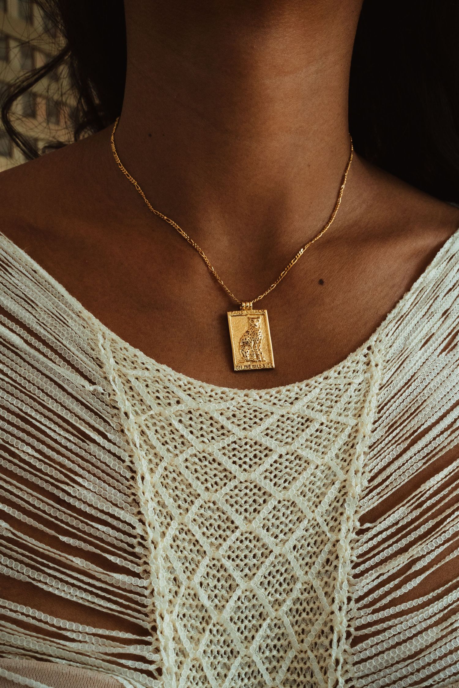 Woman wearing a gold tarot card pendant necklace with a white lace top.