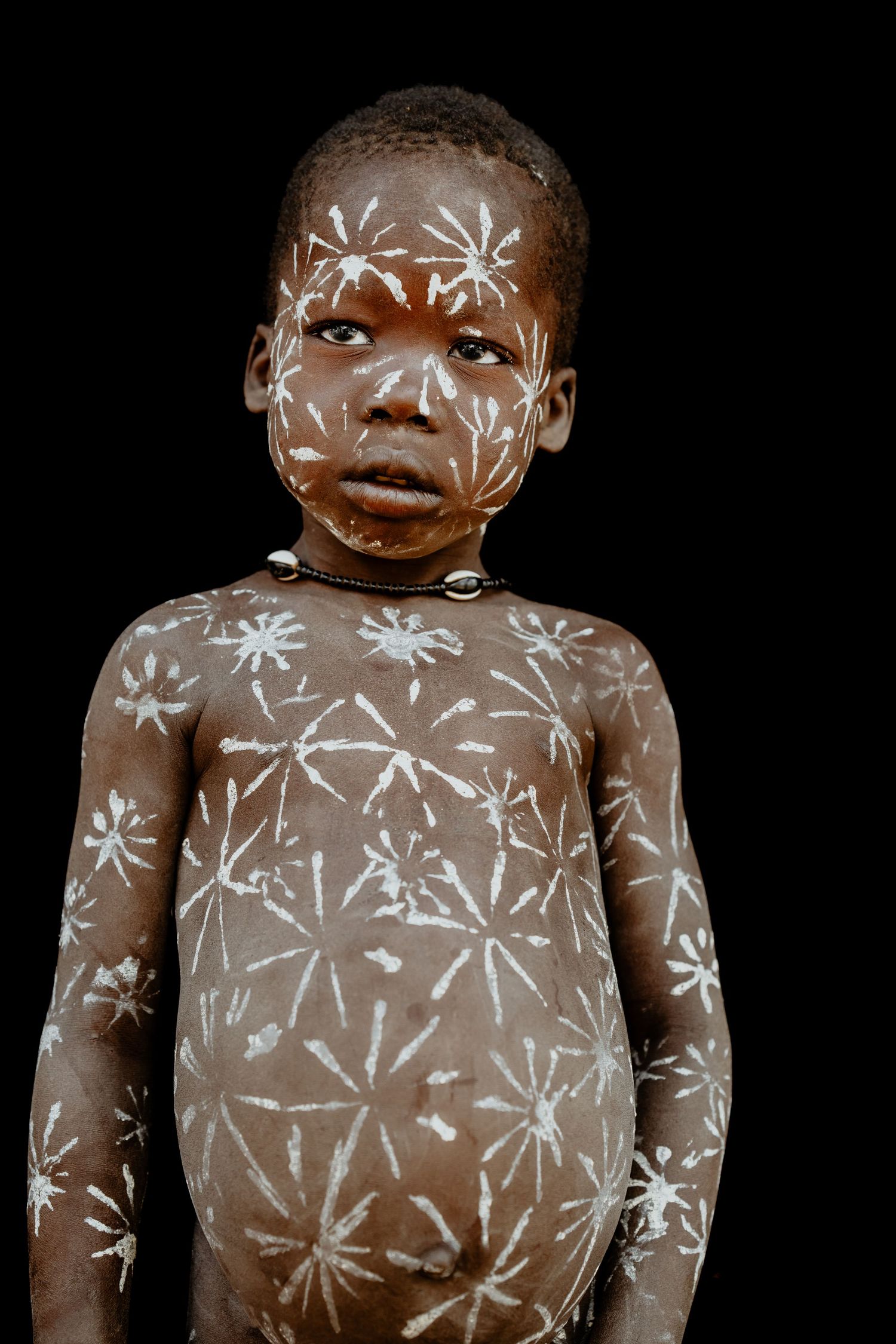 Young African child with traditional white body paint patterns on dark background.
