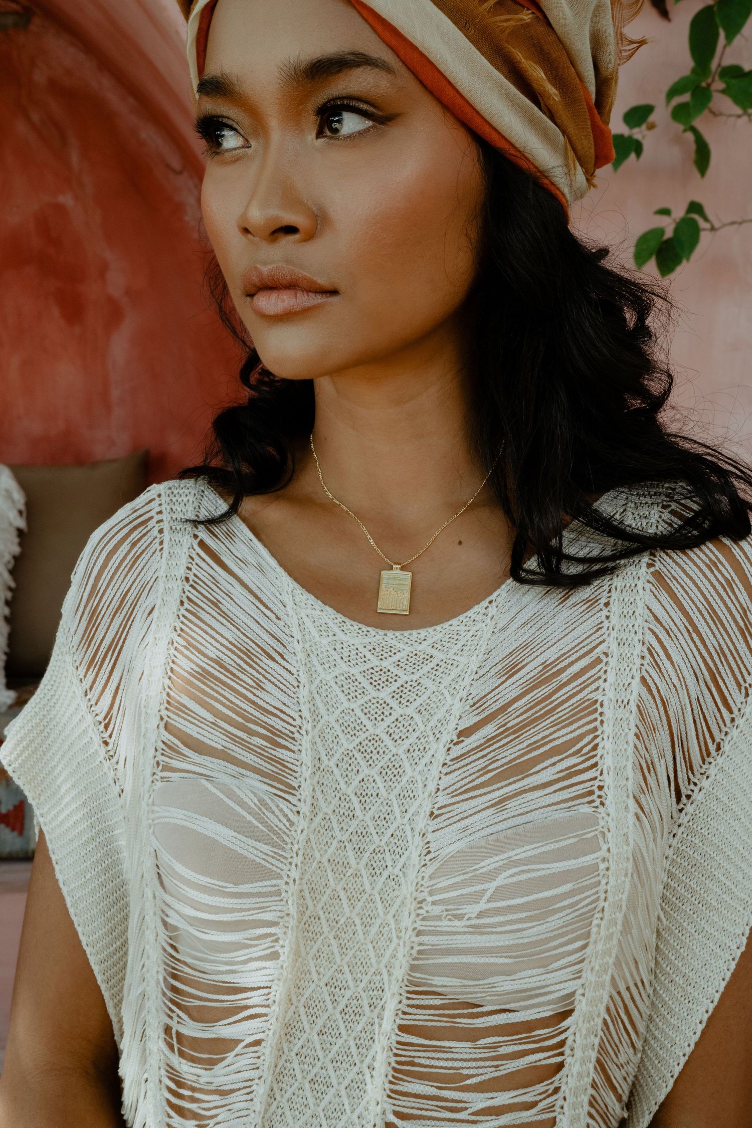 Close-up of woman in white distressed knit top wearing gold pendant necklace.