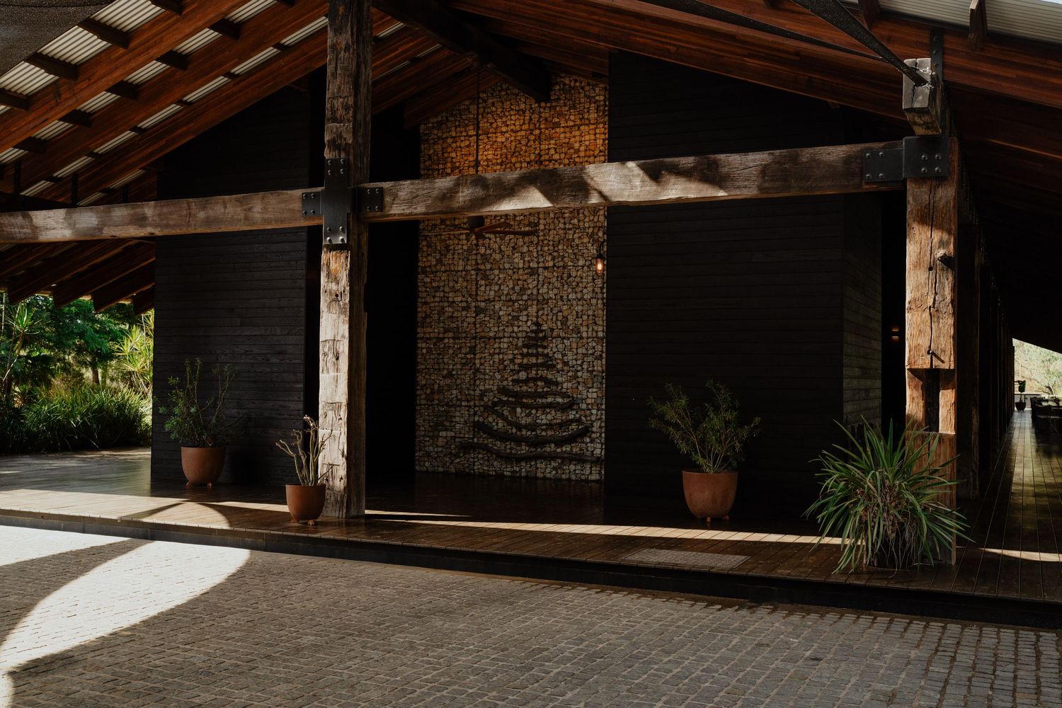 Rustic wooden pavilion entrance with decorative stone wall art and tropical plants in warm shadows.