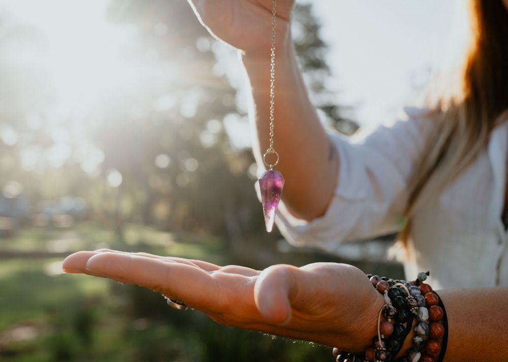 Woman holding a pink crystal pendant necklace in sunlit outdoor setting.