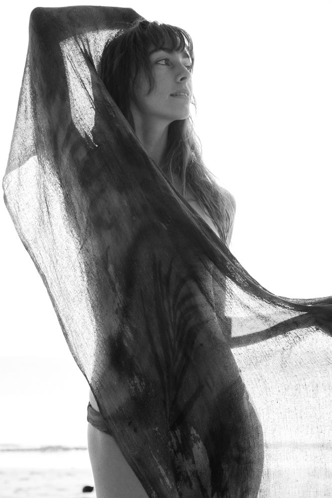 Black and white portrait of woman wrapped in sheer fabric on beach.