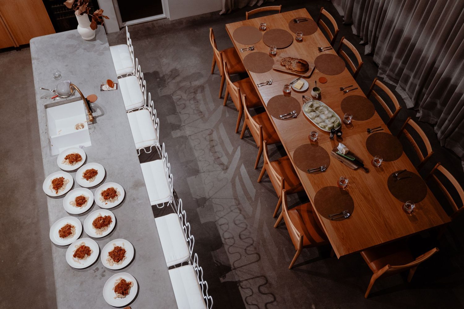 Aerial view of a long dining table set with white plates and a wooden table with place settings.