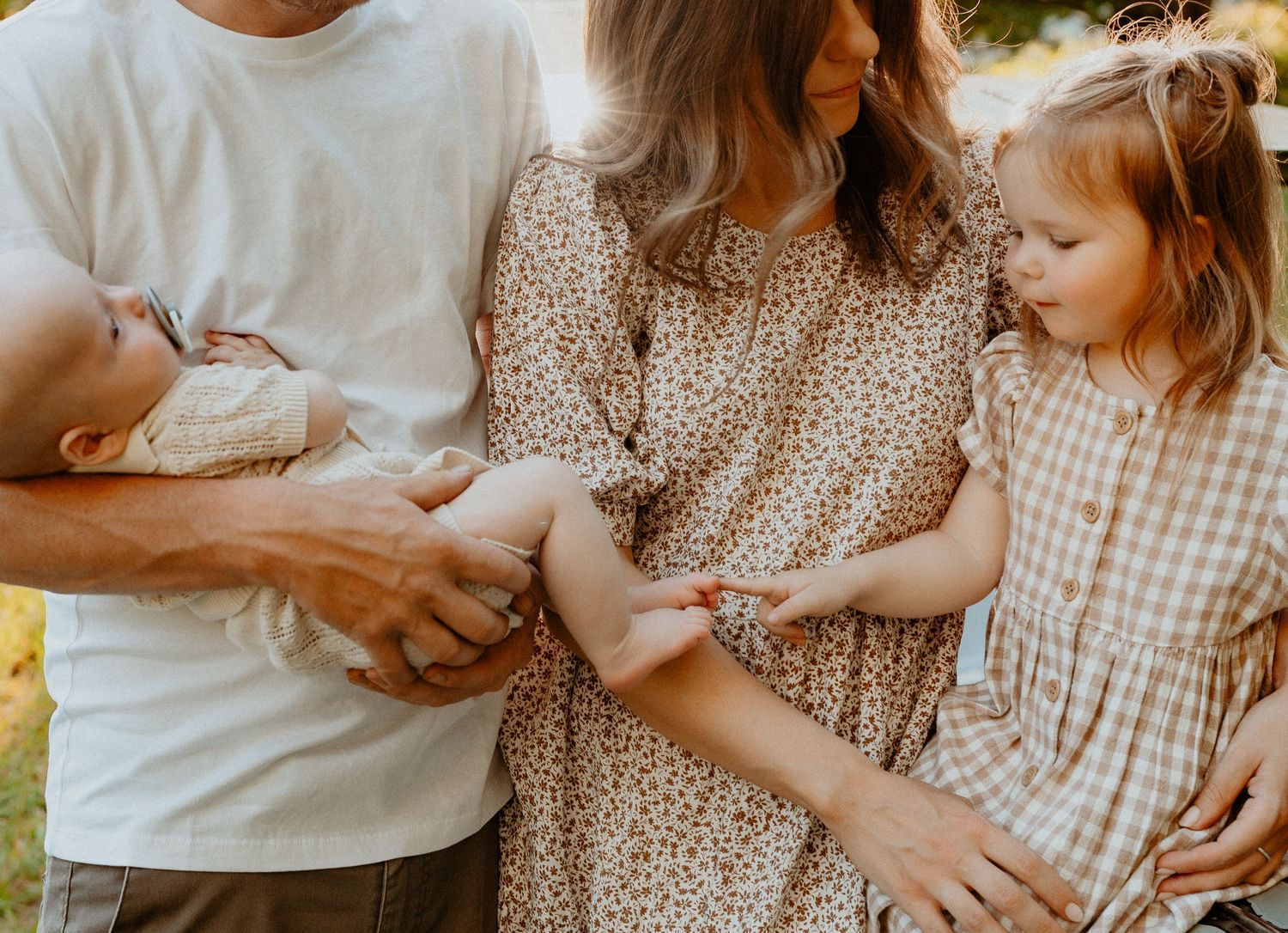 Family of four with newborn baby and toddler girl outdoors.