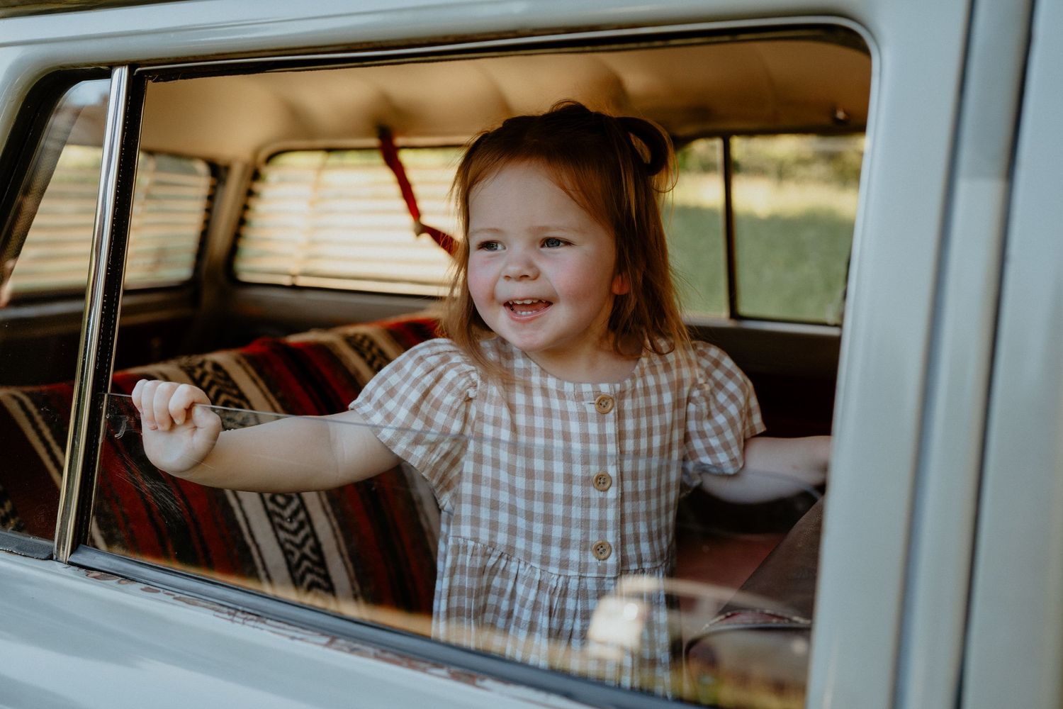 Happy toddler girl smiling and leaning out of a vintage car window.