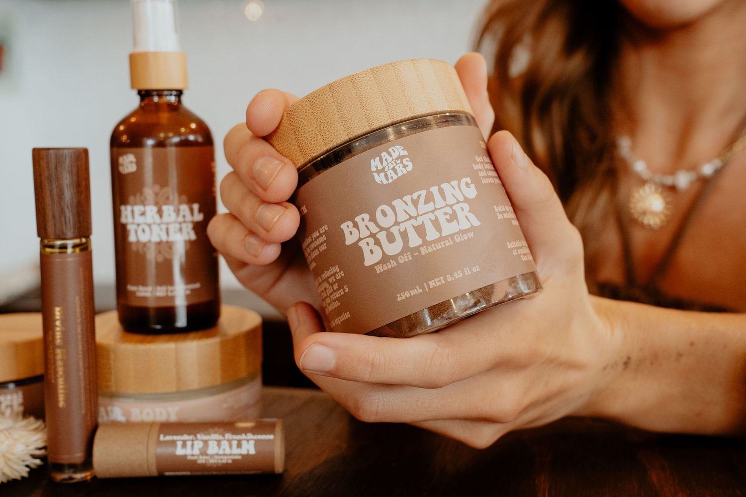 Hands holding a jar of Bronzing Butter surrounded by Herbal Tonic and Lip Balm products.