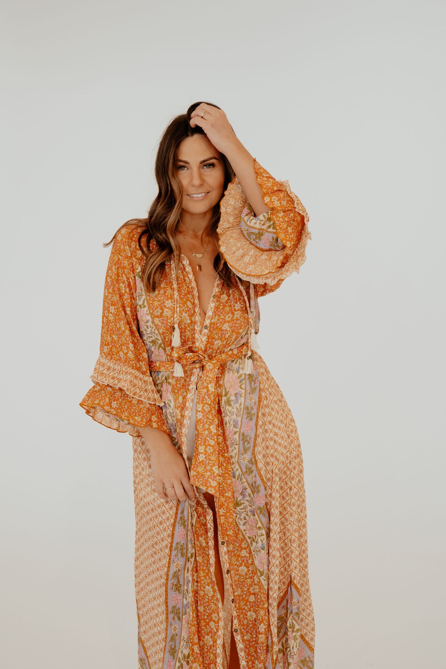 Woman wearing orange bohemian floral maxi dress with bell sleeves on white background.