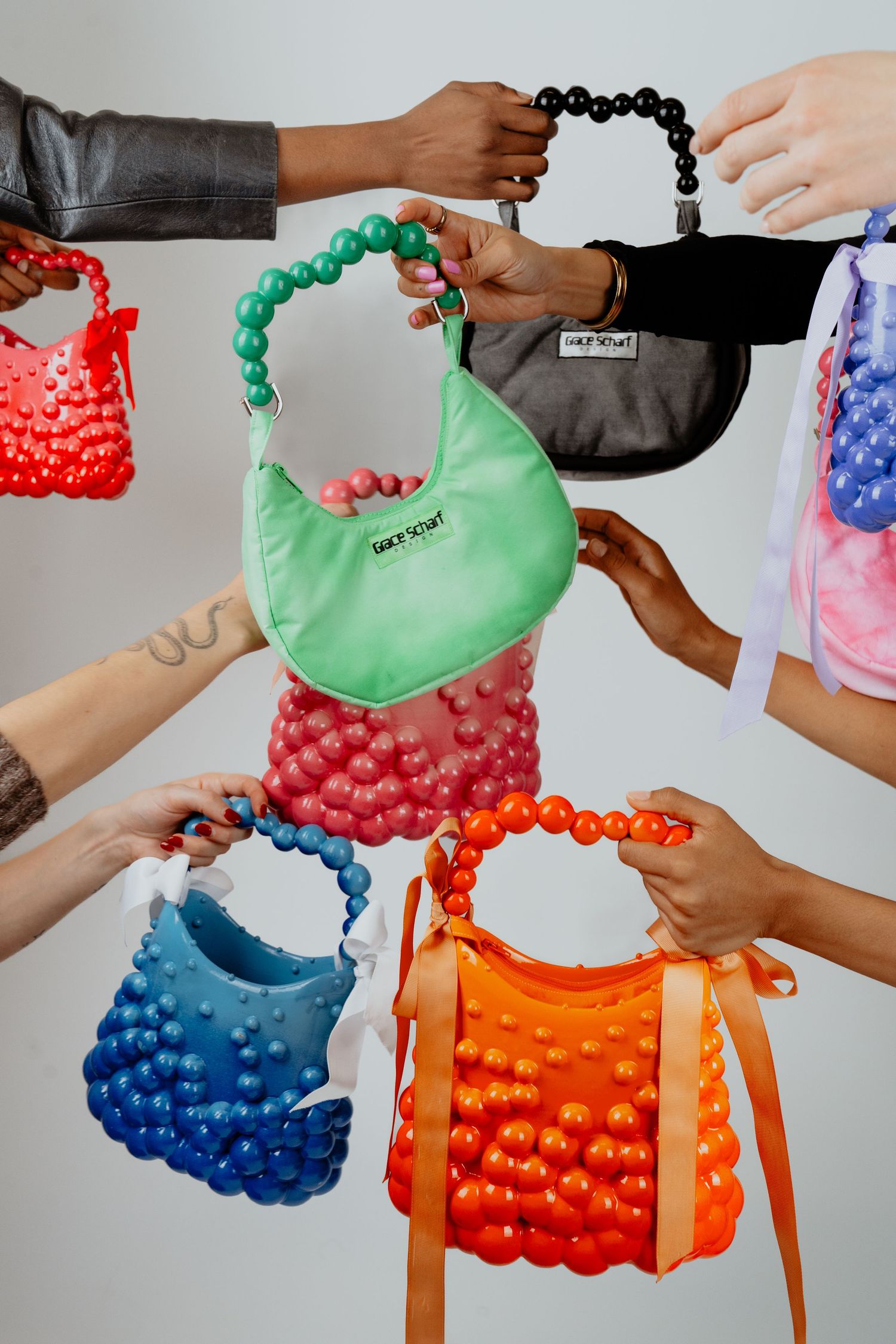 Multiple hands holding colorful beaded handbags in green, pink, blue, orange and black.