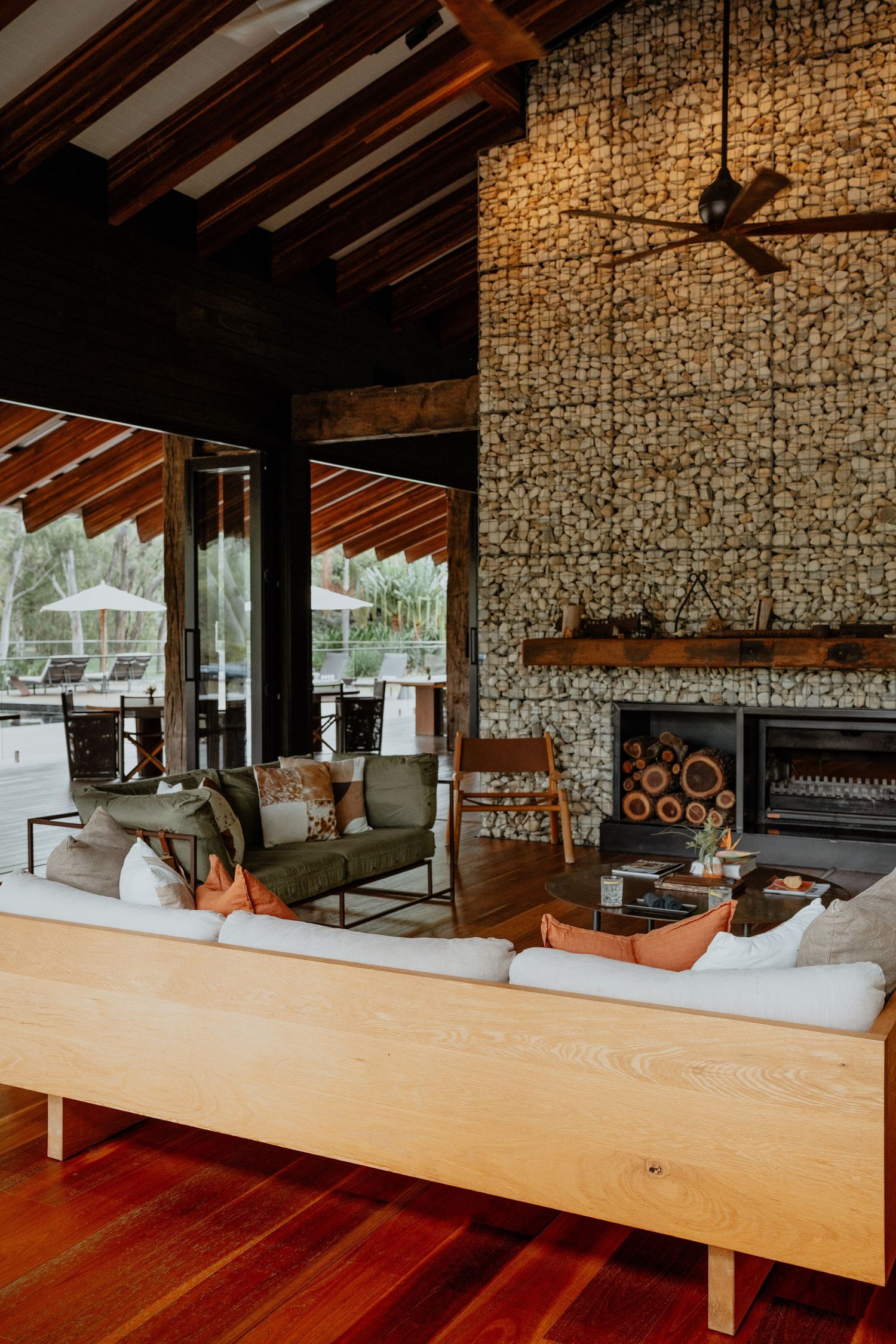 Rustic lodge interior with stone fireplace, wooden ceiling beams, and comfortable white sofas.