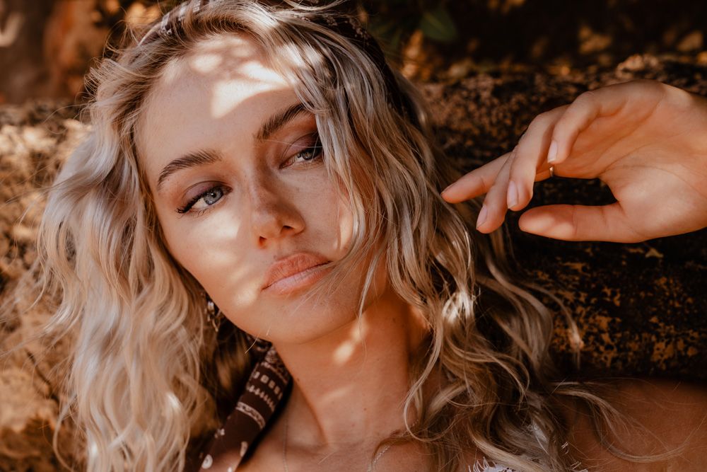Close-up of a blonde woman with wavy hair and boho jewelry in warm sunlight.