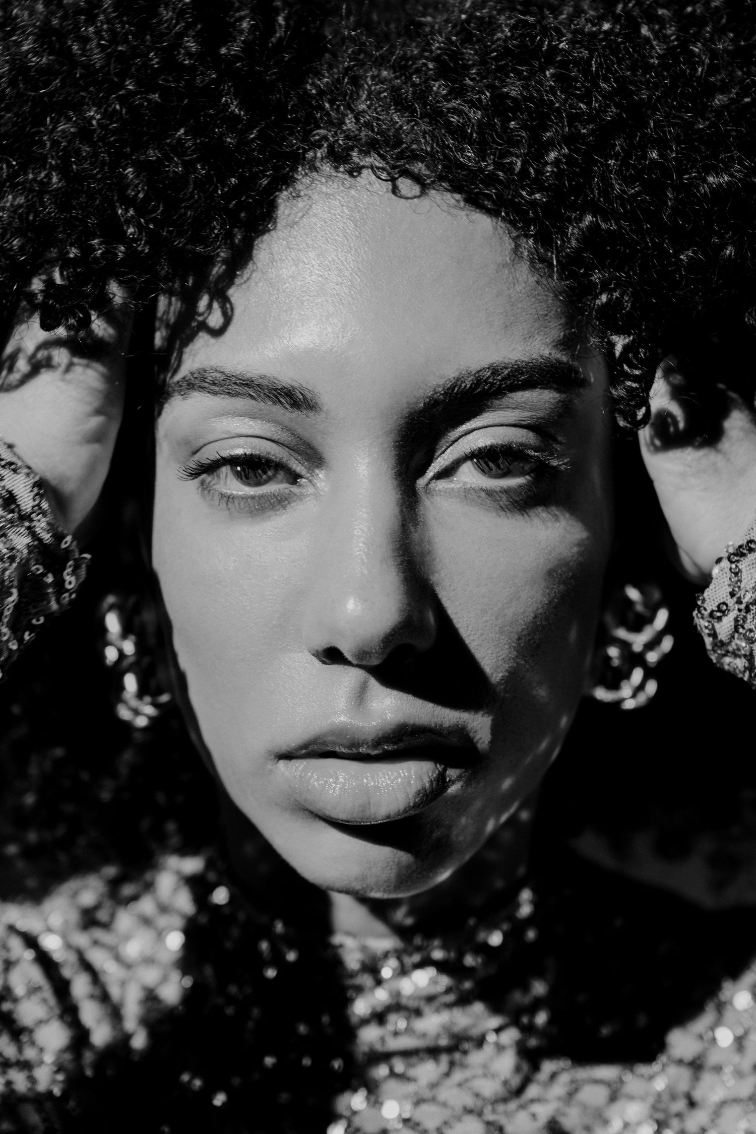 Black and white portrait of curly-haired woman with dramatic shadow lighting and hoop earrings.
