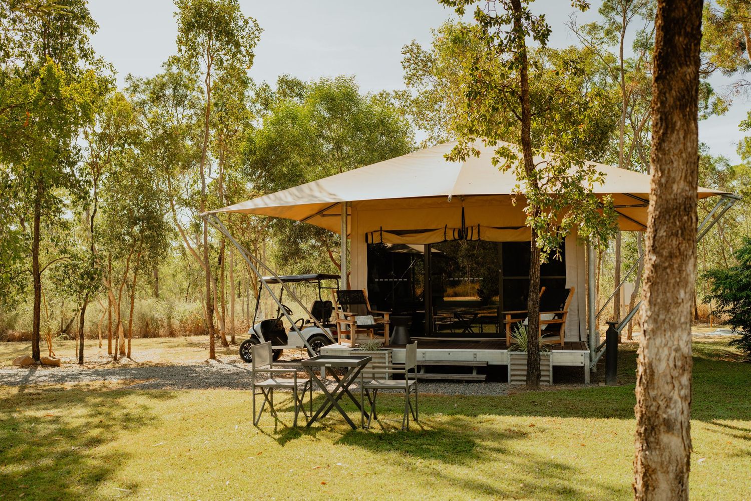 Luxury glamping tent nestled among trees with outdoor furniture on a sunny day.