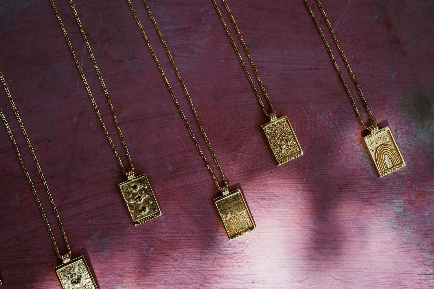 Five gold tarot card pendant necklaces laid flat on a purple wooden surface.