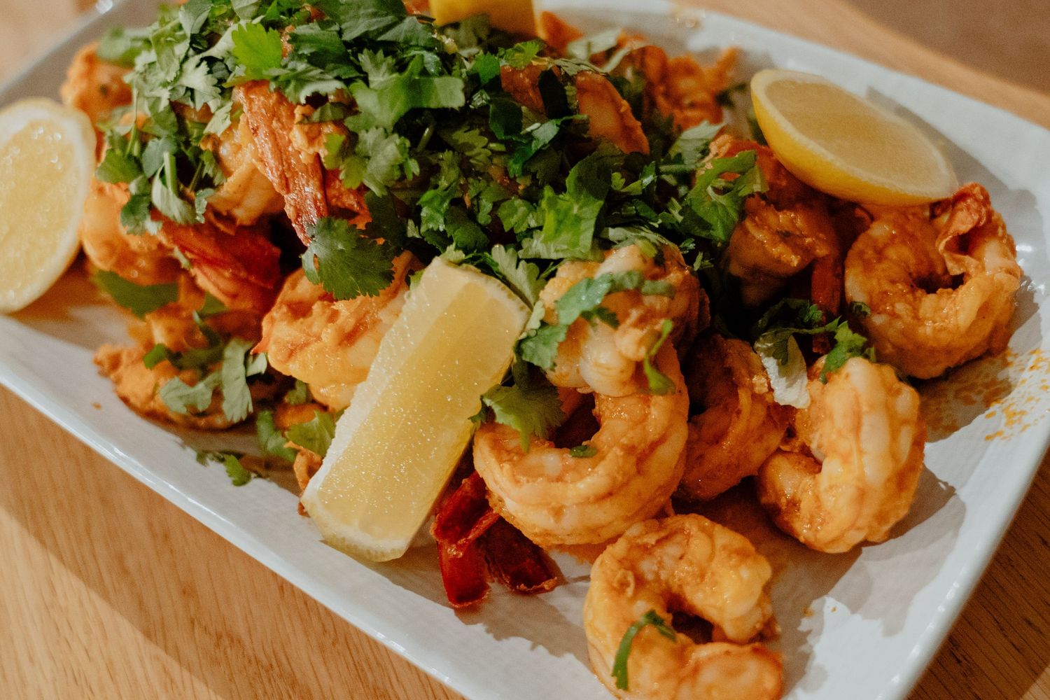 Spiced shrimp platter garnished with fresh cilantro and lemon wedges on a white plate.