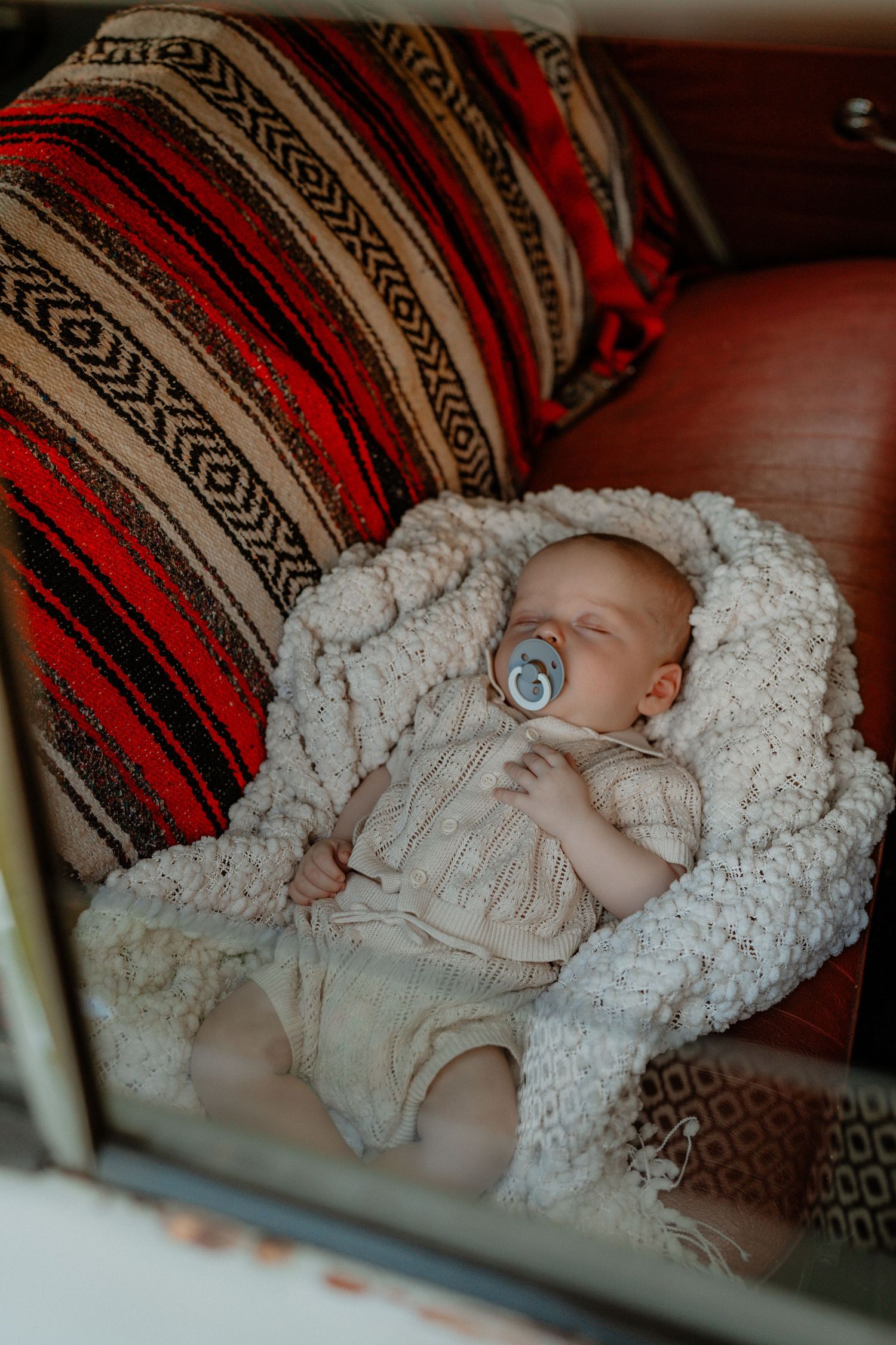 Sleeping newborn baby with pacifier wrapped in a knit blanket inside a vintage car.