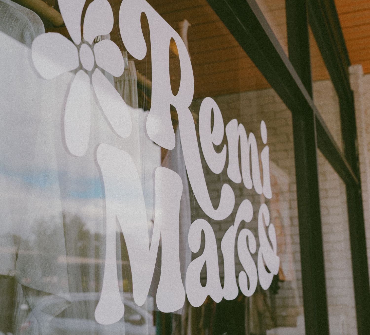 White retro-style Remi Mars logo decal on a storefront window with bokeh background.