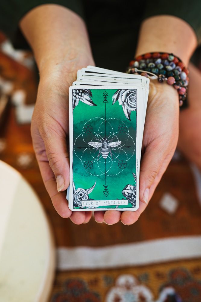 Hands holding a green tarot deck featuring a bee and pentacle design.