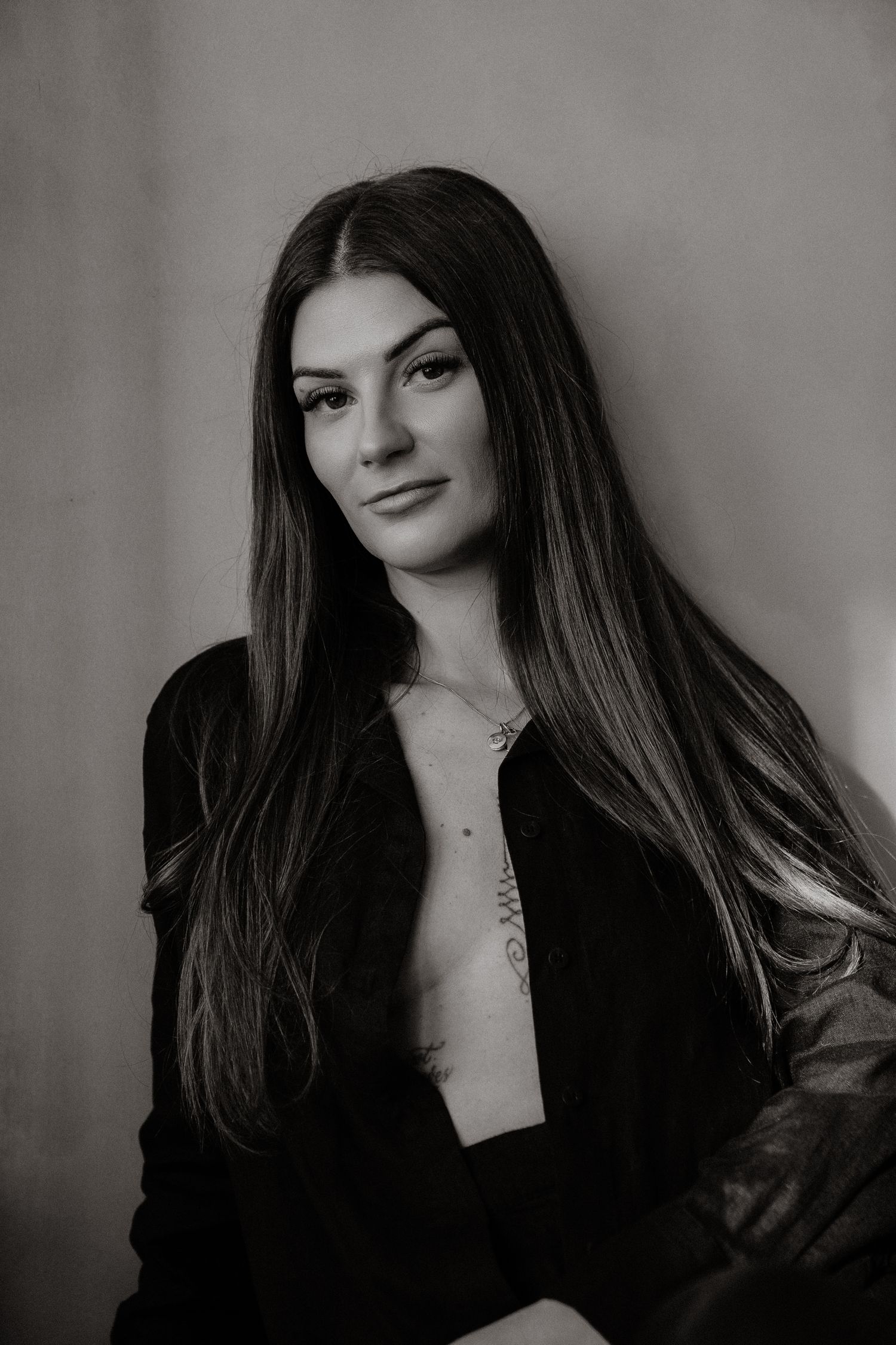 Black and white portrait of a young woman with long dark hair wearing an open black jacket indoors.
