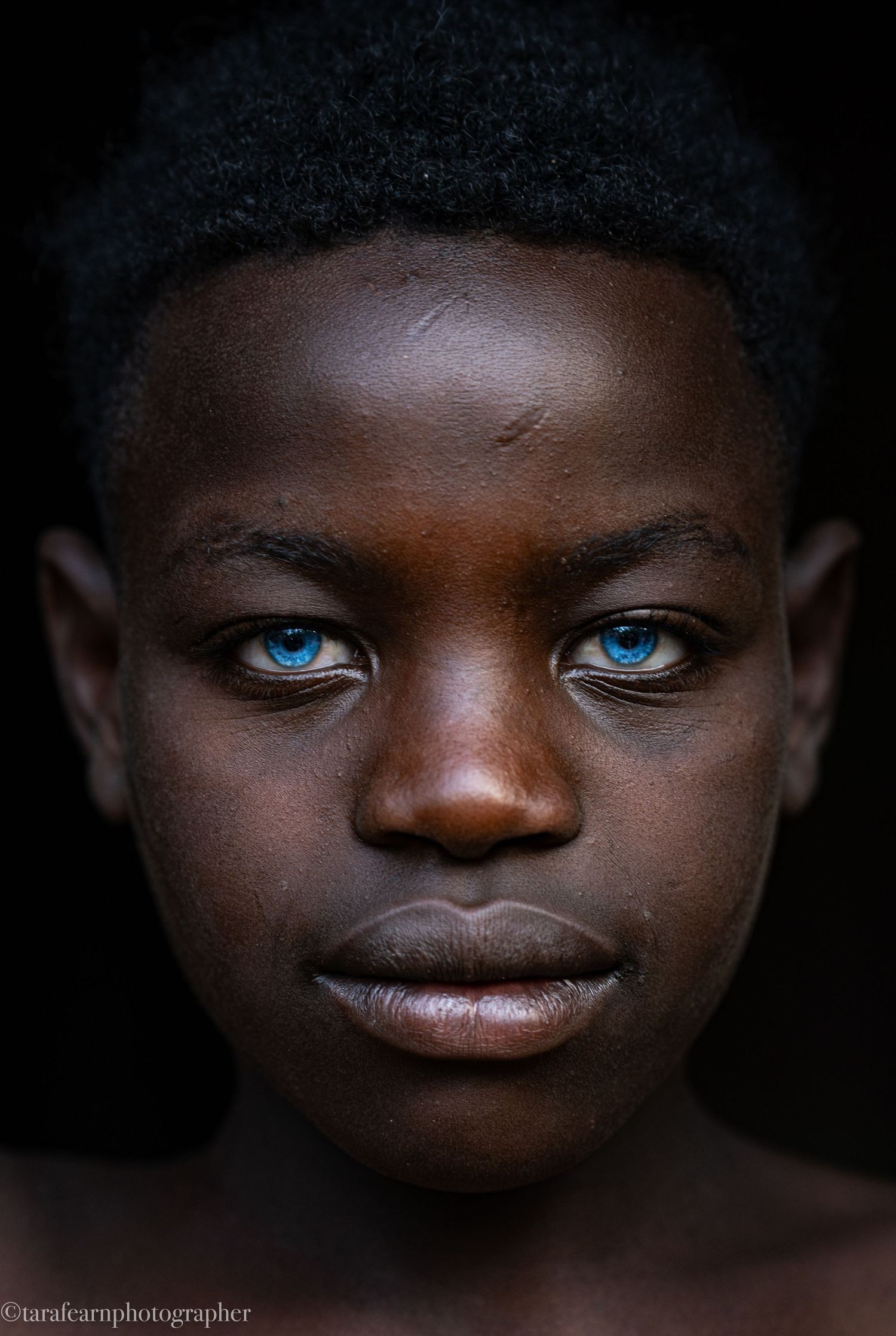 Close-up portrait of a young man with striking blue eyes against a dark background.