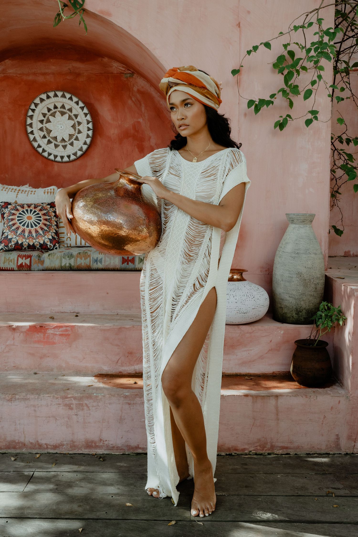Woman in white fringe maxi dress holding copper bowl in Moroccan setting.